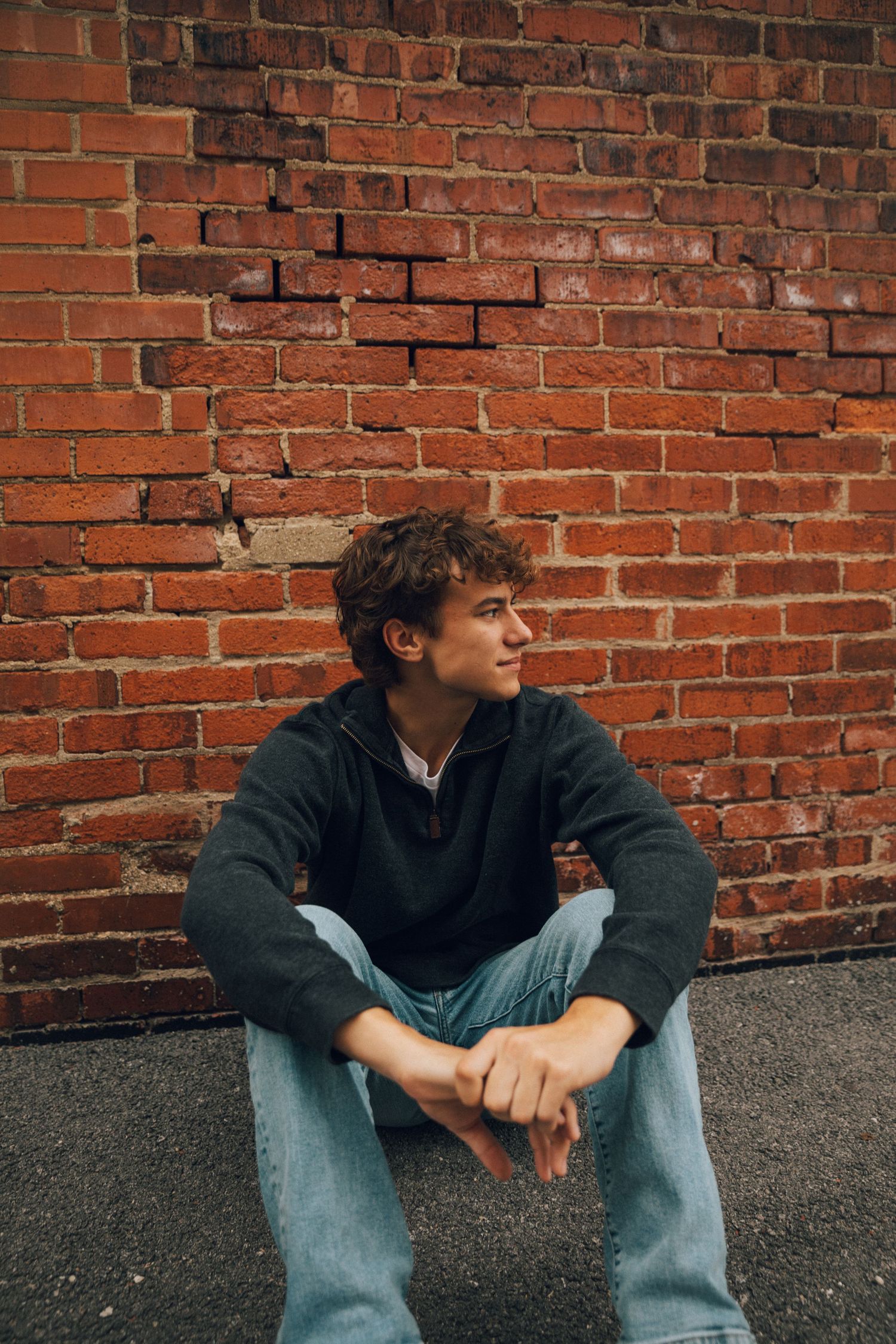 A relaxed portrait against textured red brick wall in natural lighting.