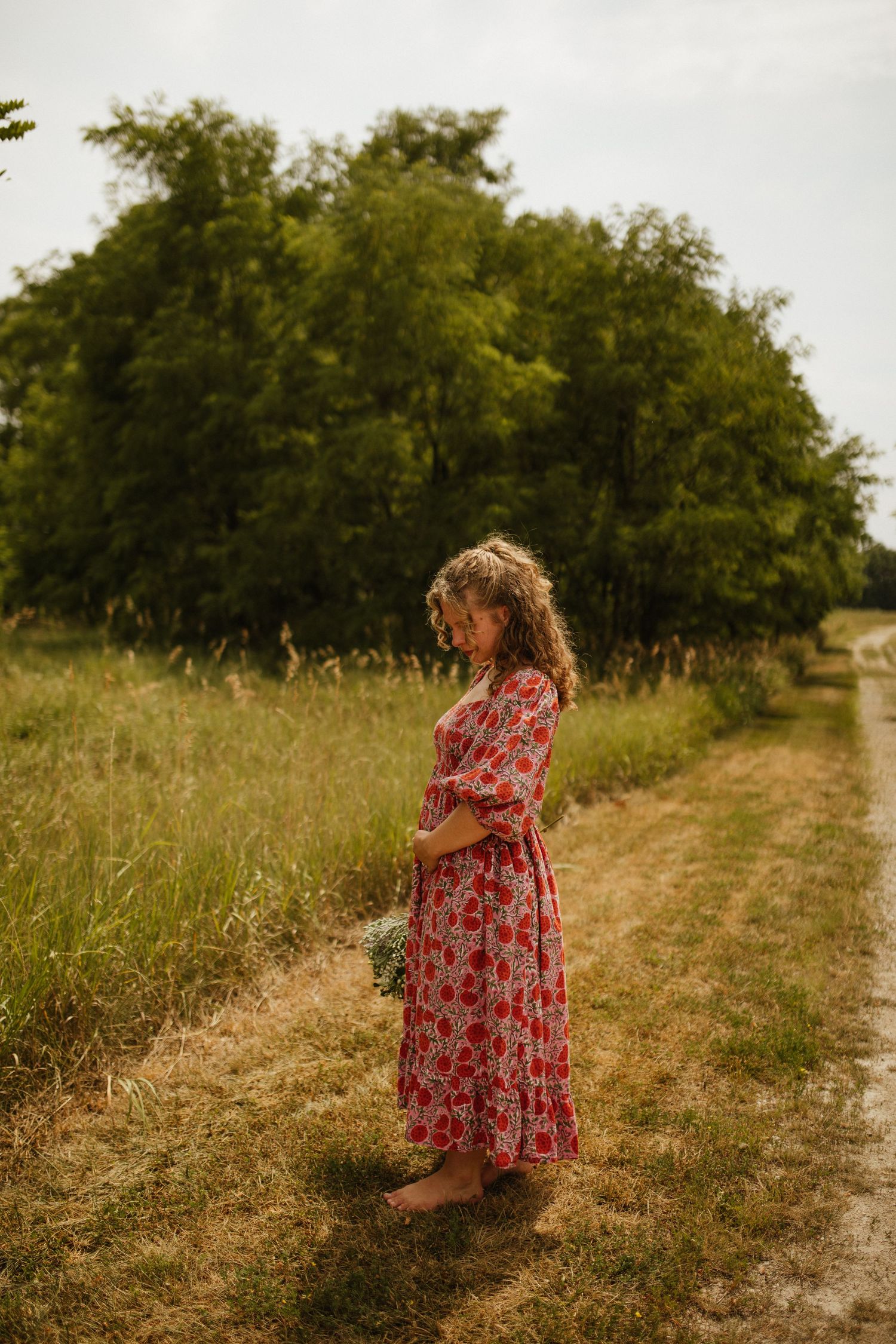 Person in red floral dress walking through golden field on sunny day.