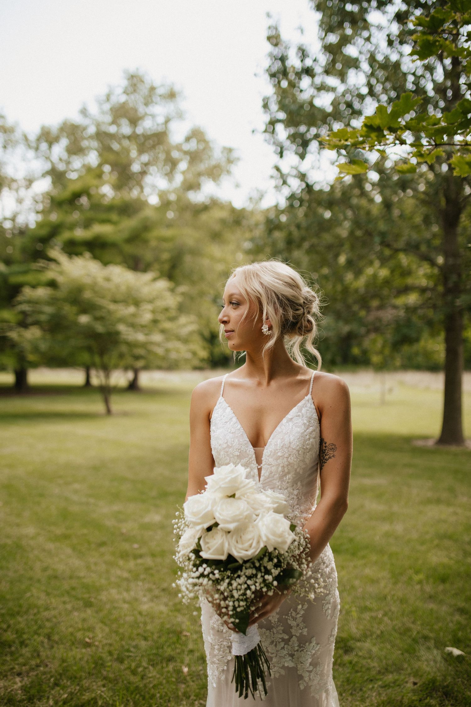 Bride in lace dress holding white floral bouquet poses in garden setting.