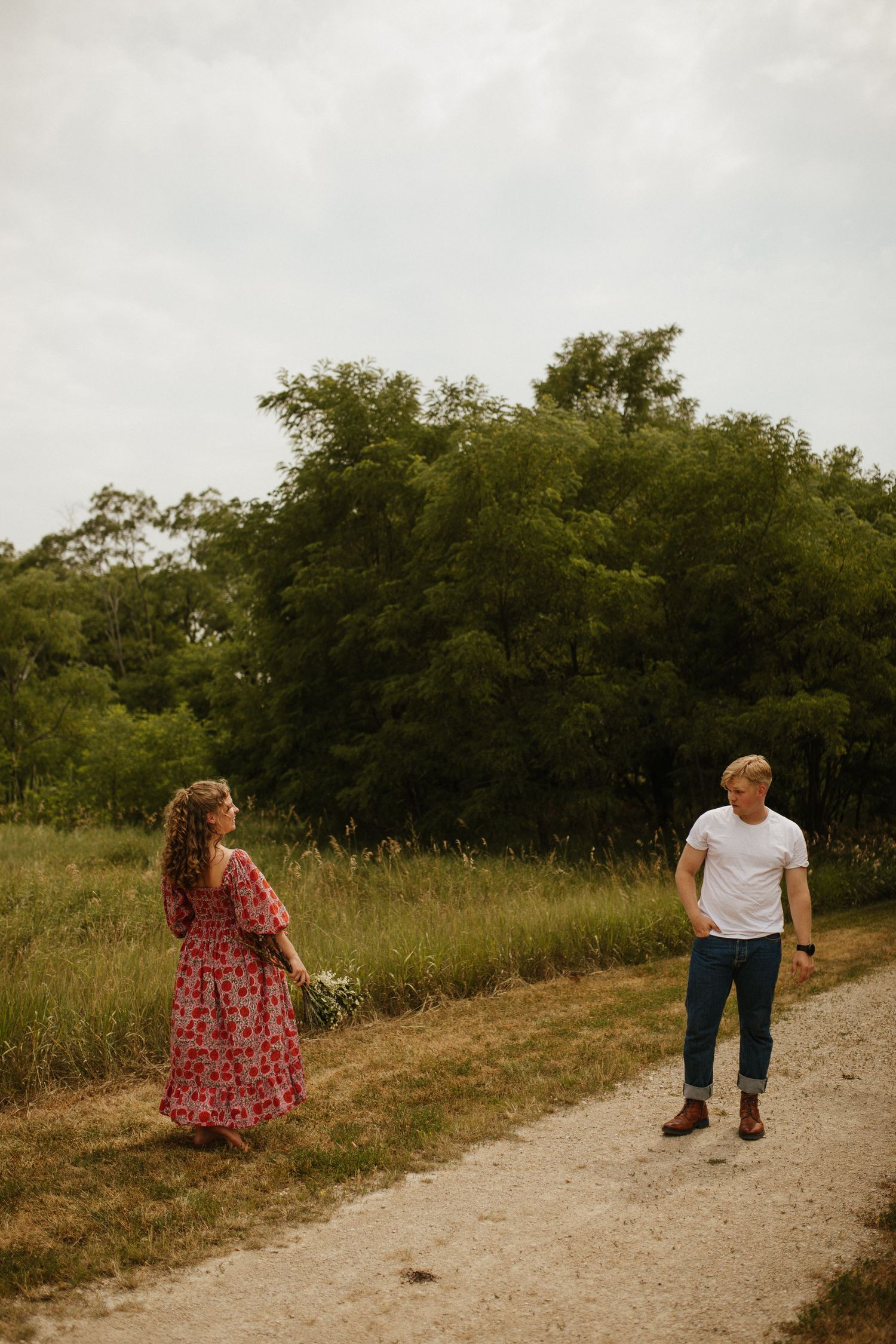 Two people walking together on rural gravel path with trees in background.