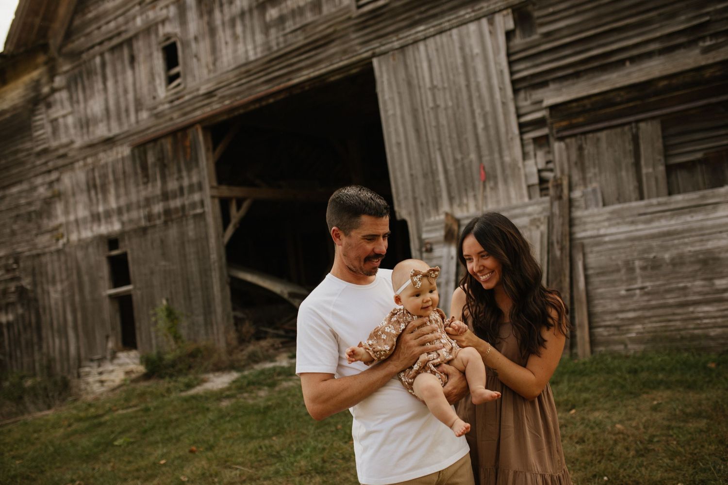 Romantic couple sharing intimate moments in front of a rustic wooden barn at sunset.