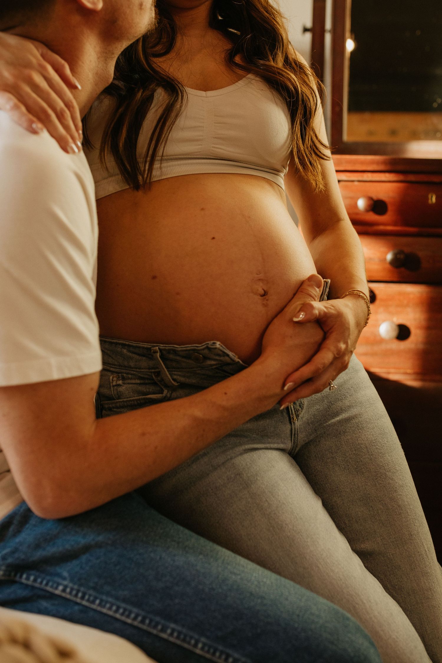 Intimate maternity photo showing hands cradling a pregnant belly in natural light.