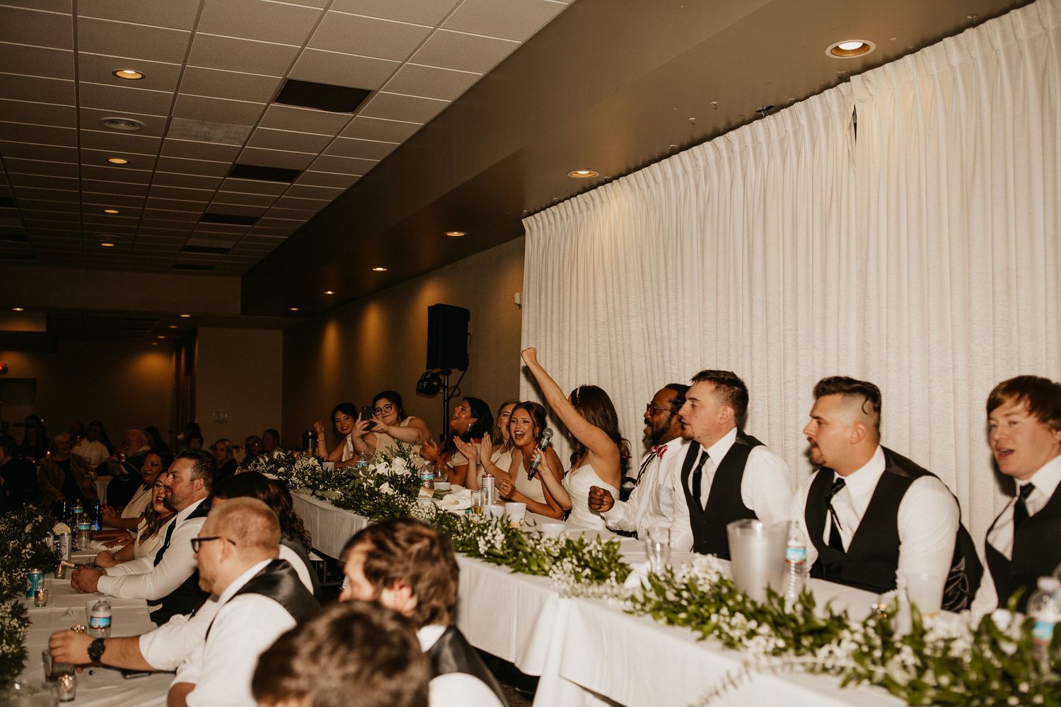 Wedding reception venue with white draping and floral centerpieces on dining tables.