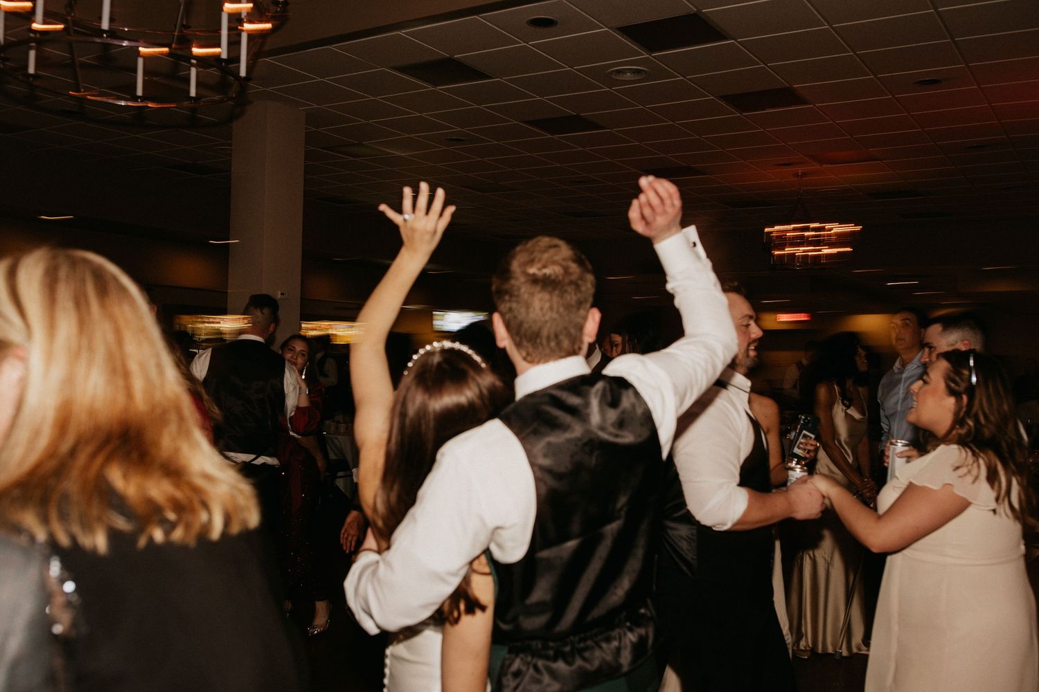 Wedding reception party with guests dancing and celebrating on a dark dance floor.
