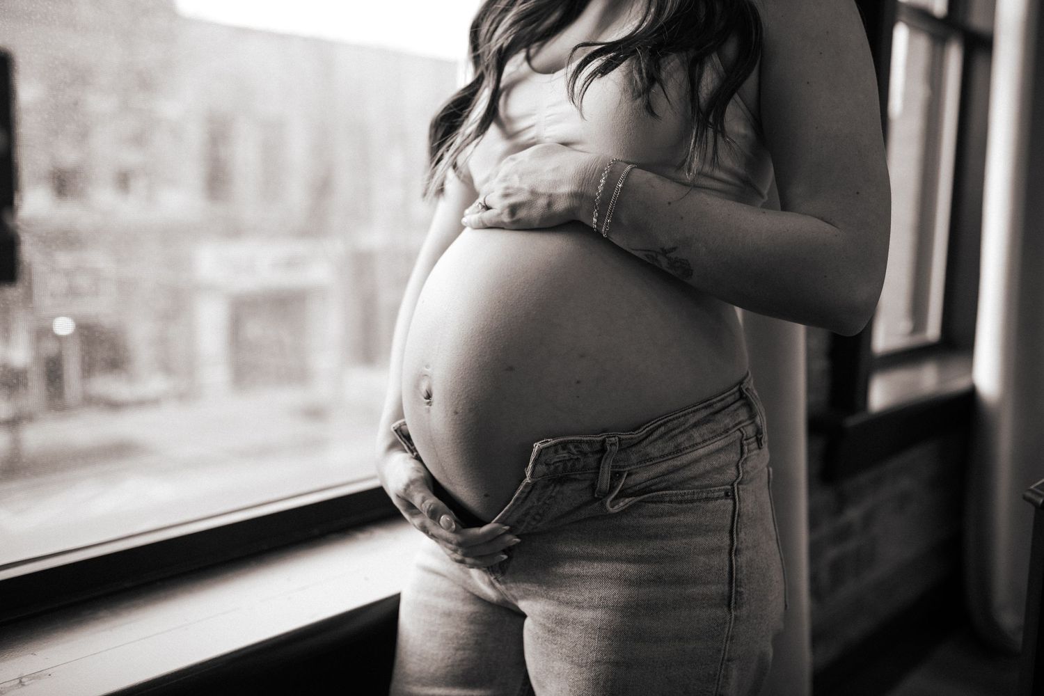 Black and white photo of pregnant belly being cradled near a window.