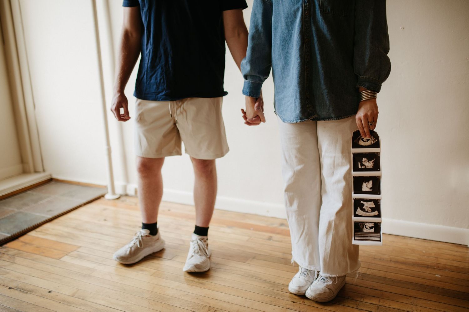 Couple's feet and legs shown on hardwood floor during indoor photo session.