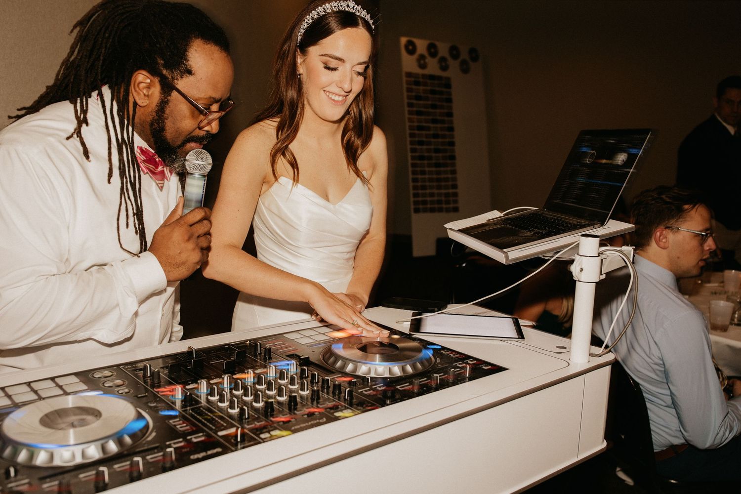 DJ and guest collaborate at the mixing deck during a wedding reception celebration.