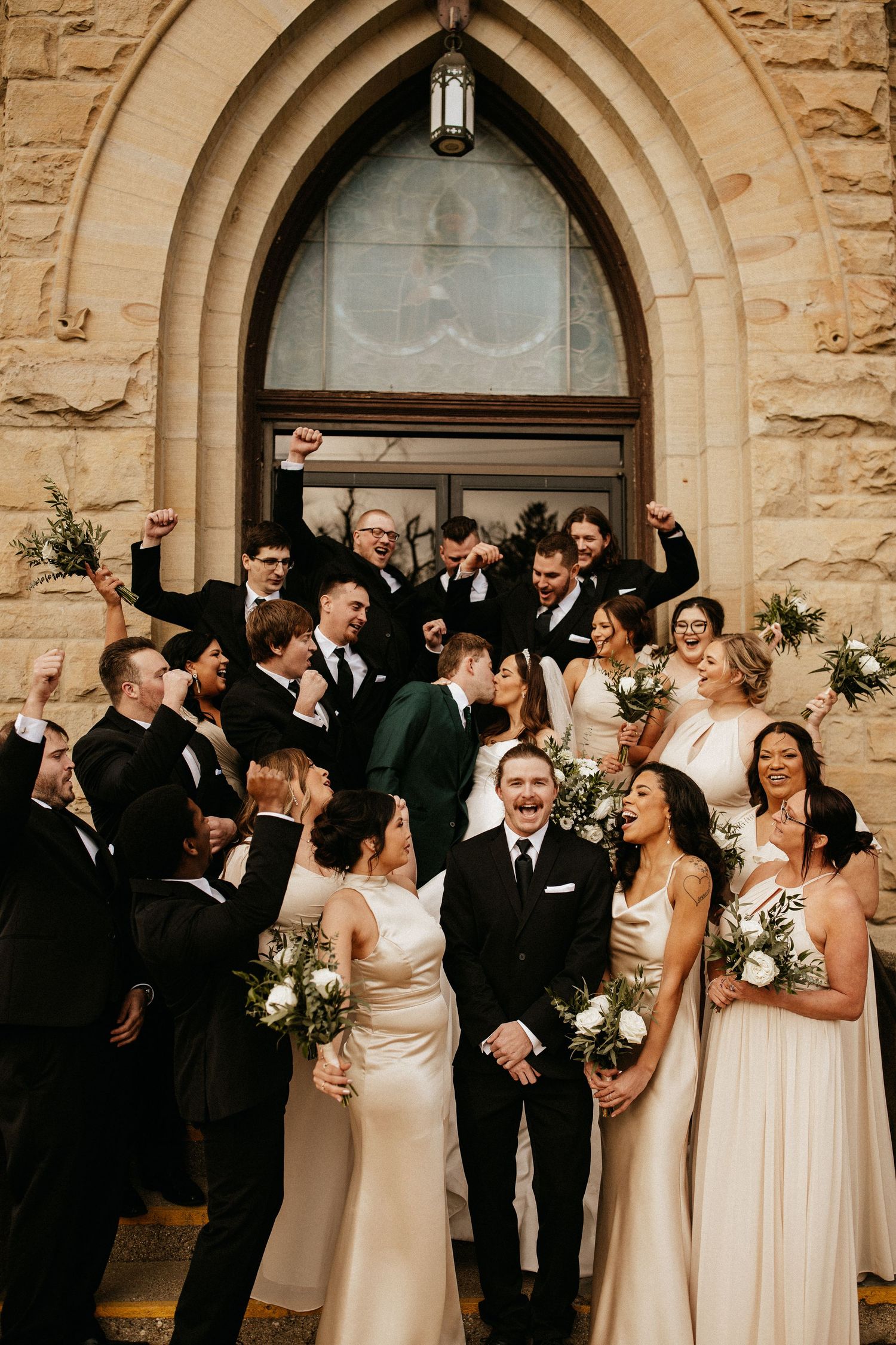 Wedding party celebrates outside historic stone church with gothic arched doorways.