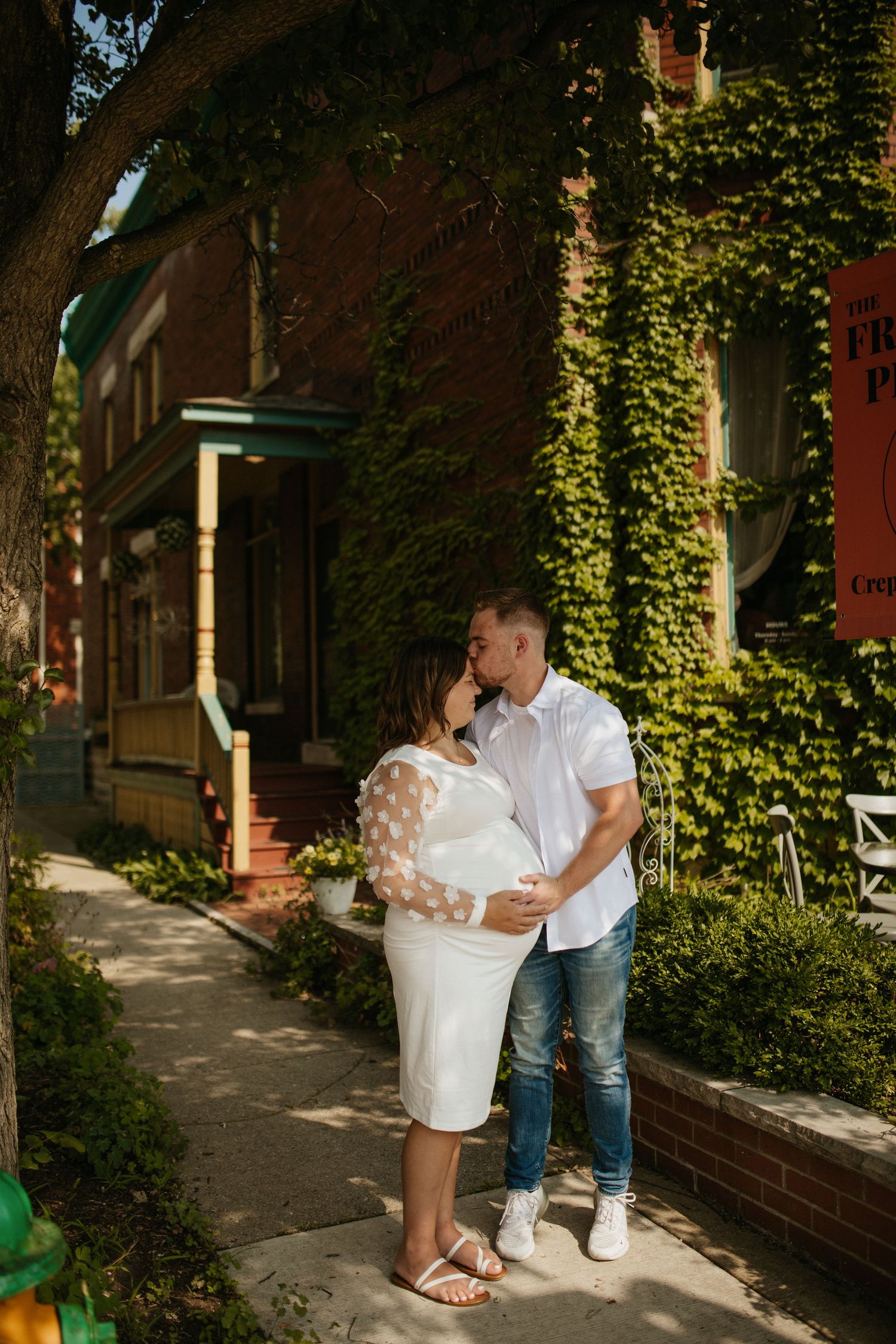 Couple embracing near ivy-covered brick building in sunlight.