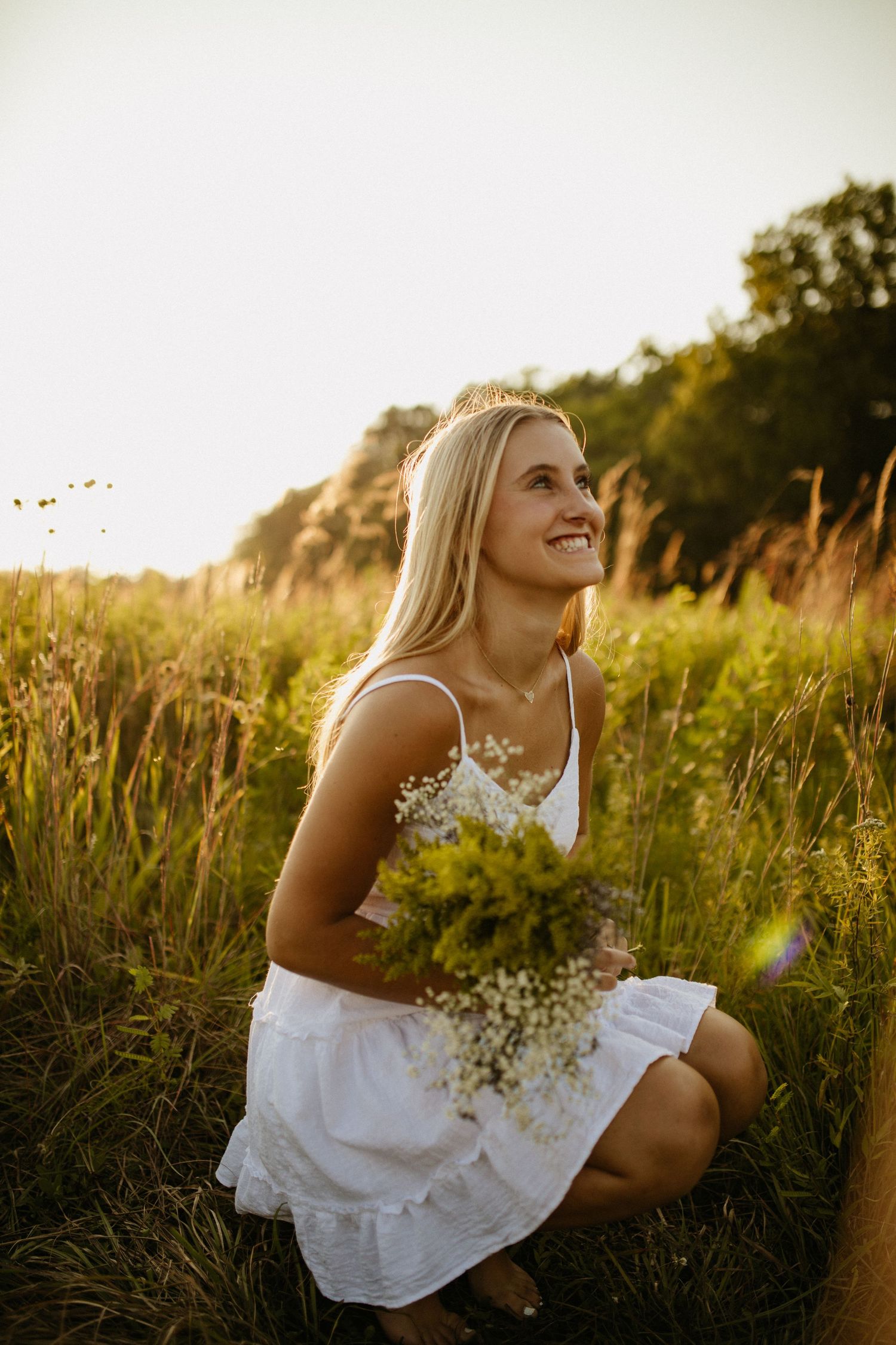 Person in white dress sits among wildflowers during golden hour.