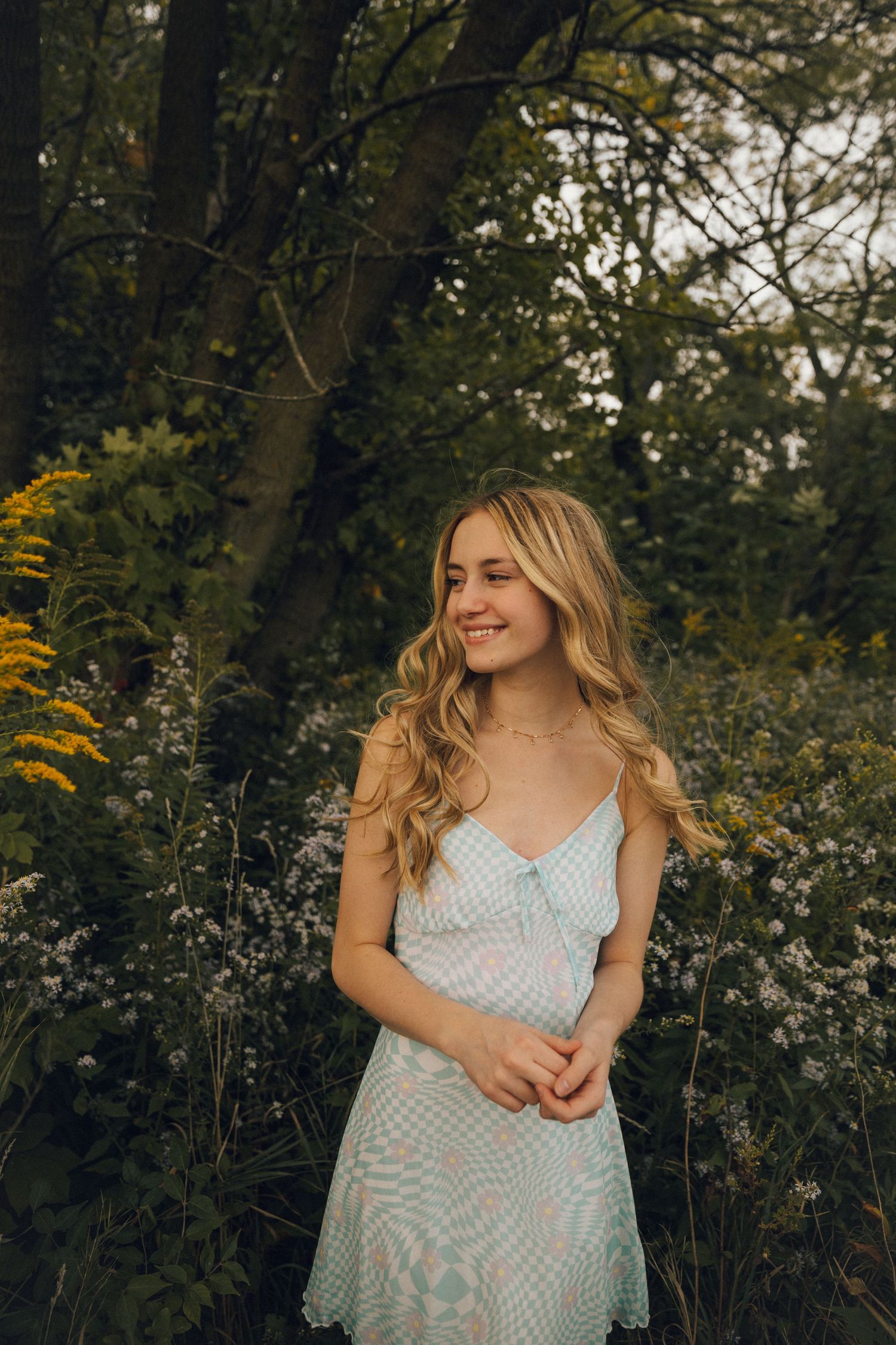 A natural outdoor portrait featuring a woman in a light blue dress among flowering plants.
