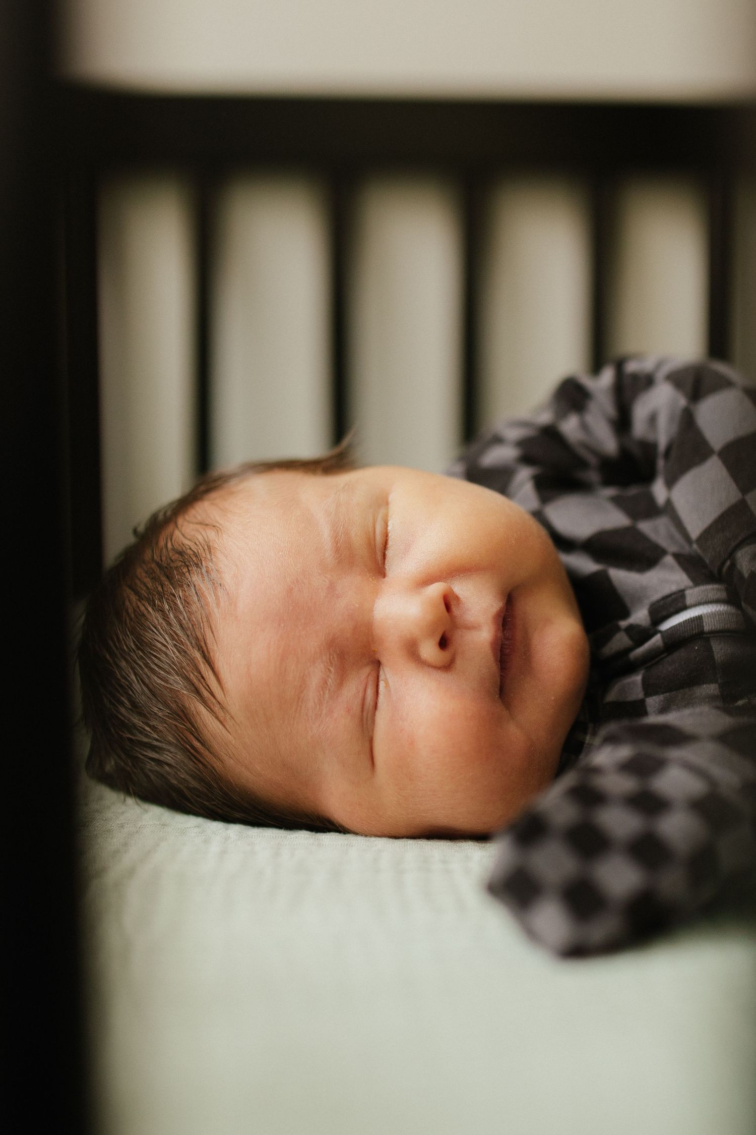 Artistic black and white portrait of a sleeping infant through crib slats.