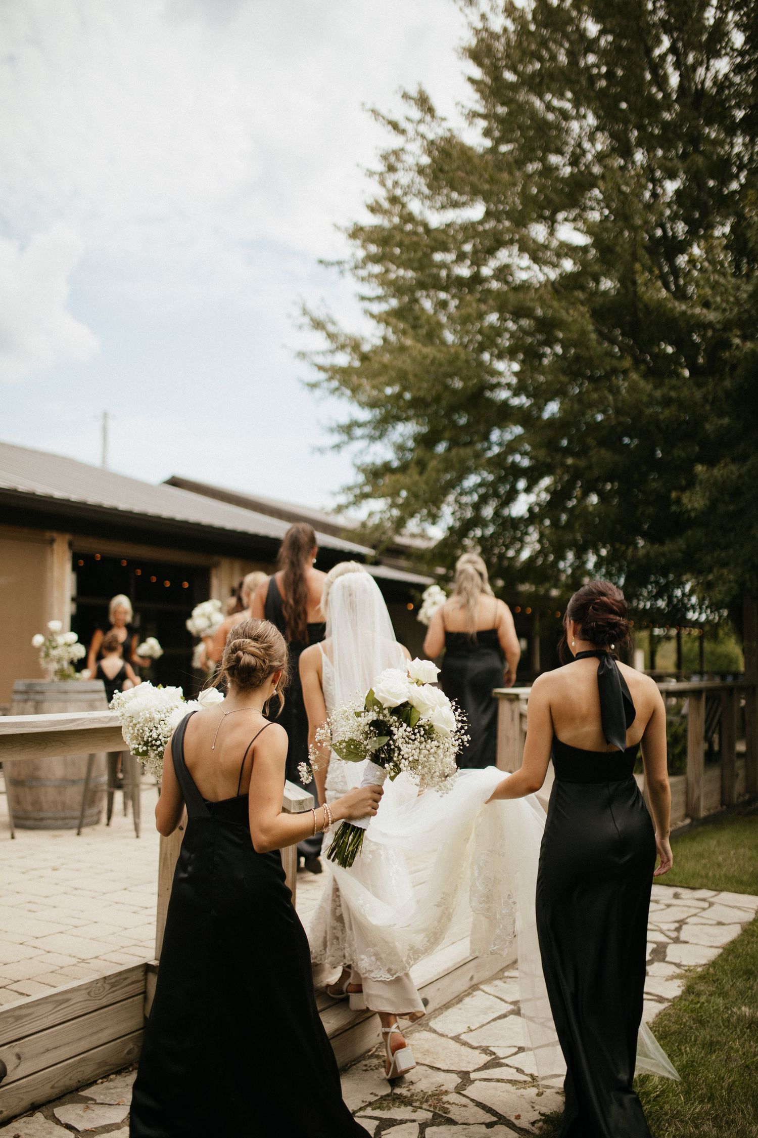 Bridesmaids in black dresses walking together outdoors during wedding festivities.