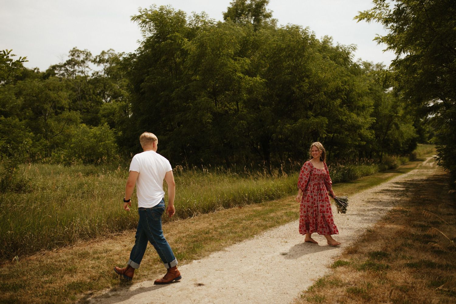 Two people walking on dirt path through natural grassland area.