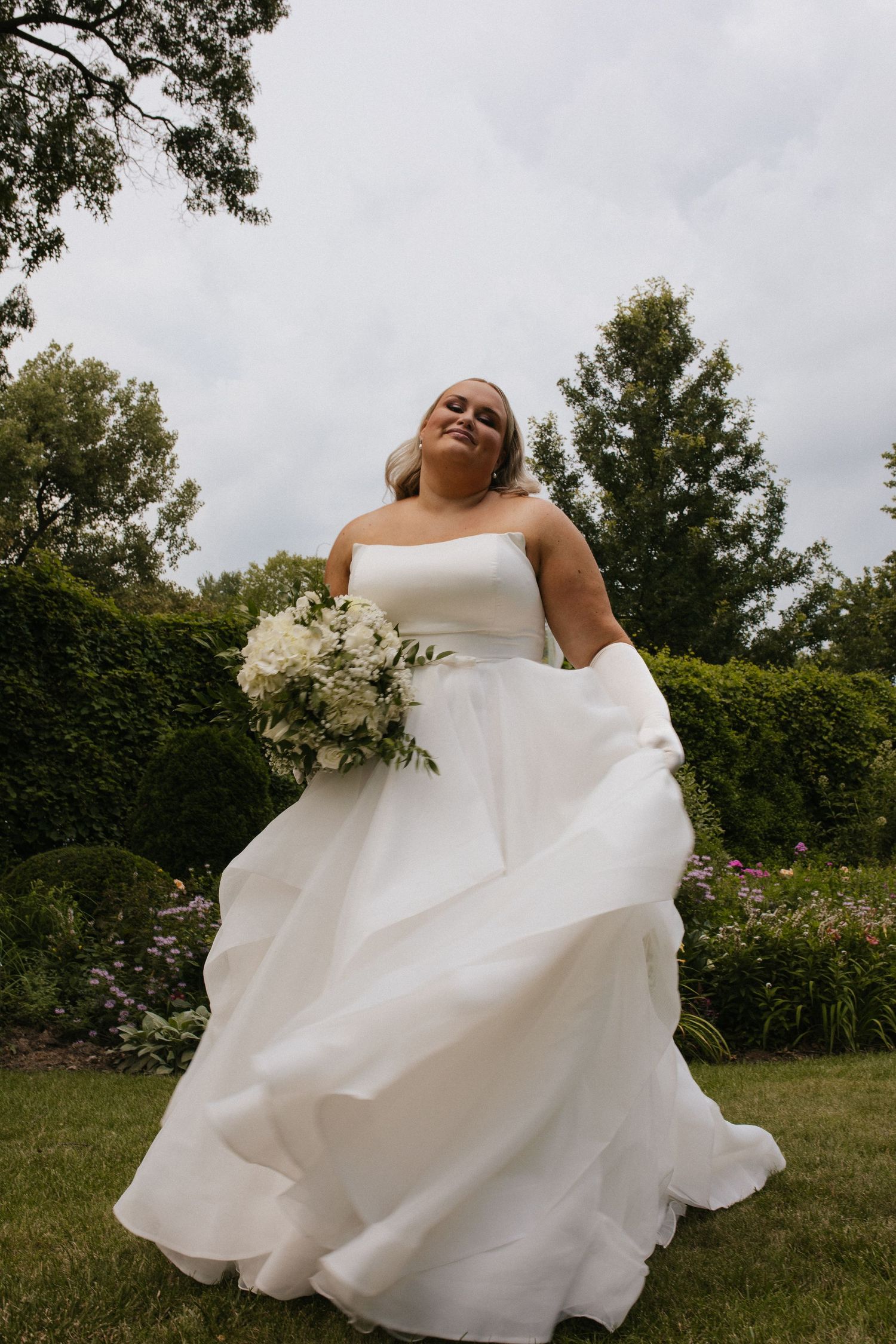 Flowing white wedding dress captured in motion against garden landscape.