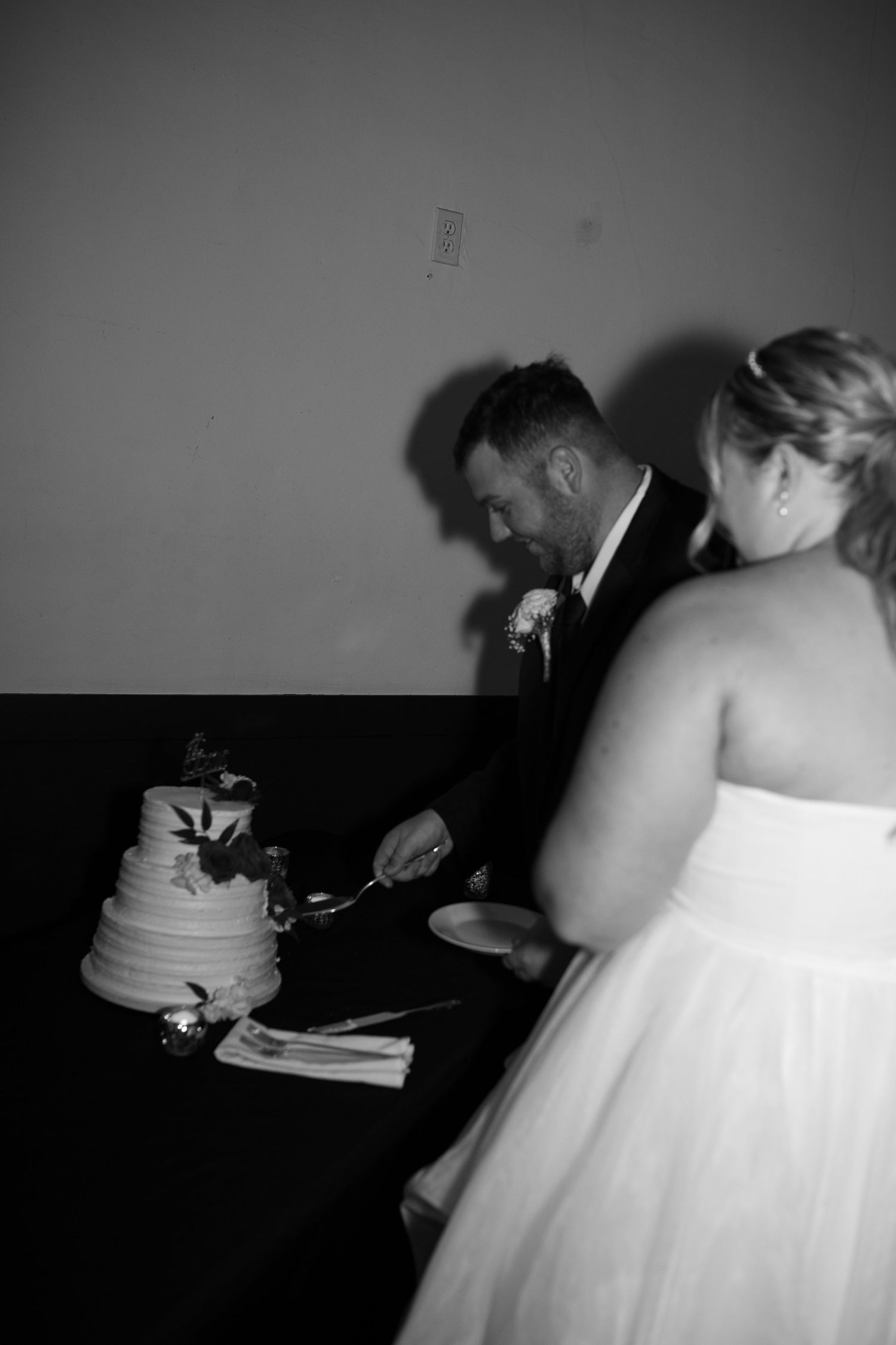 A black and white photo of a couple cutting their wedding cake together.