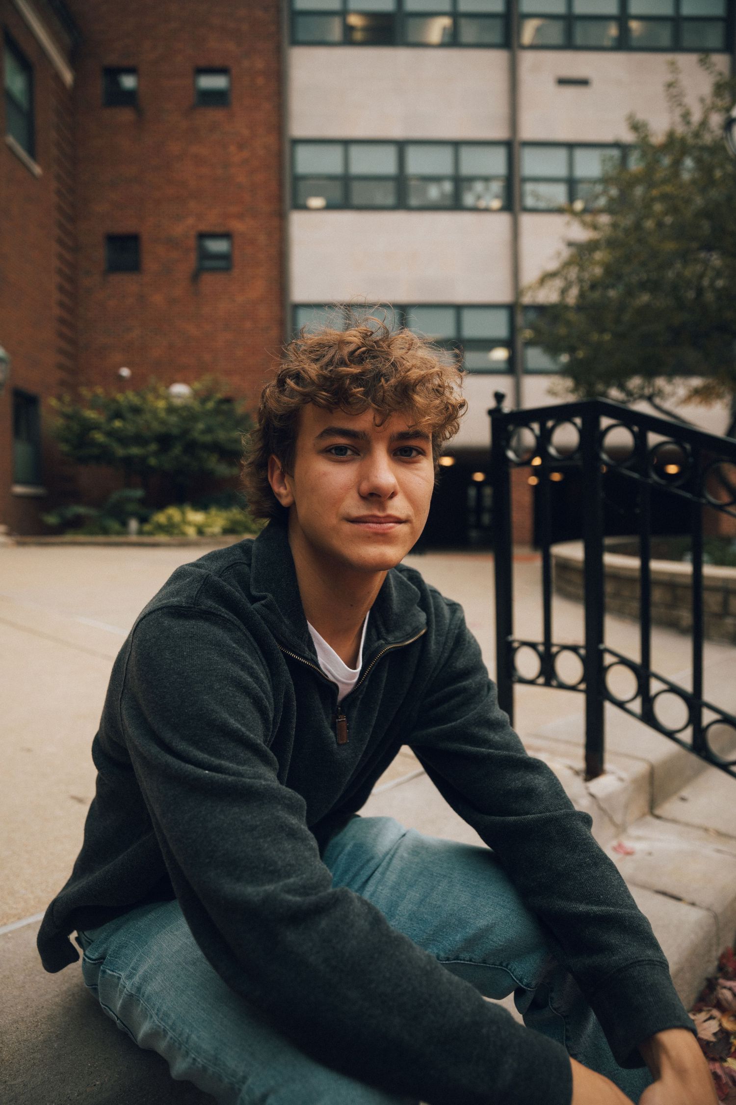 Person in fleece jacket poses on brick steps near campus building.