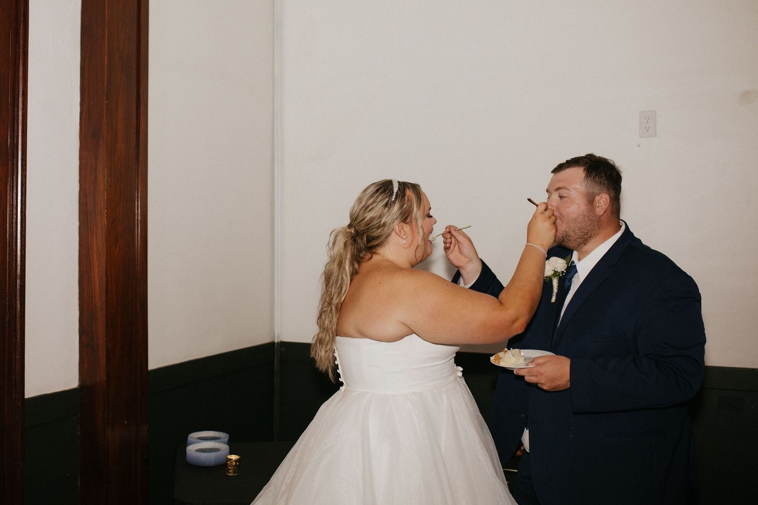 A couple shares a playful moment while feeding each other cake at their wedding reception.