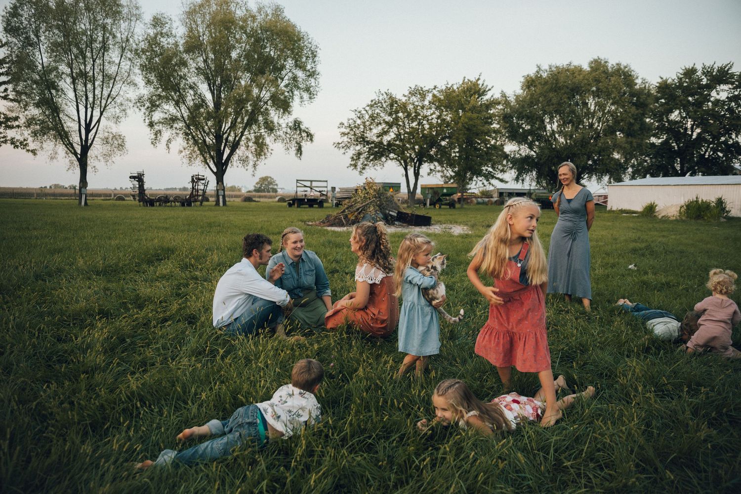 A group gathers for a picnic on grass near trees at sunset.