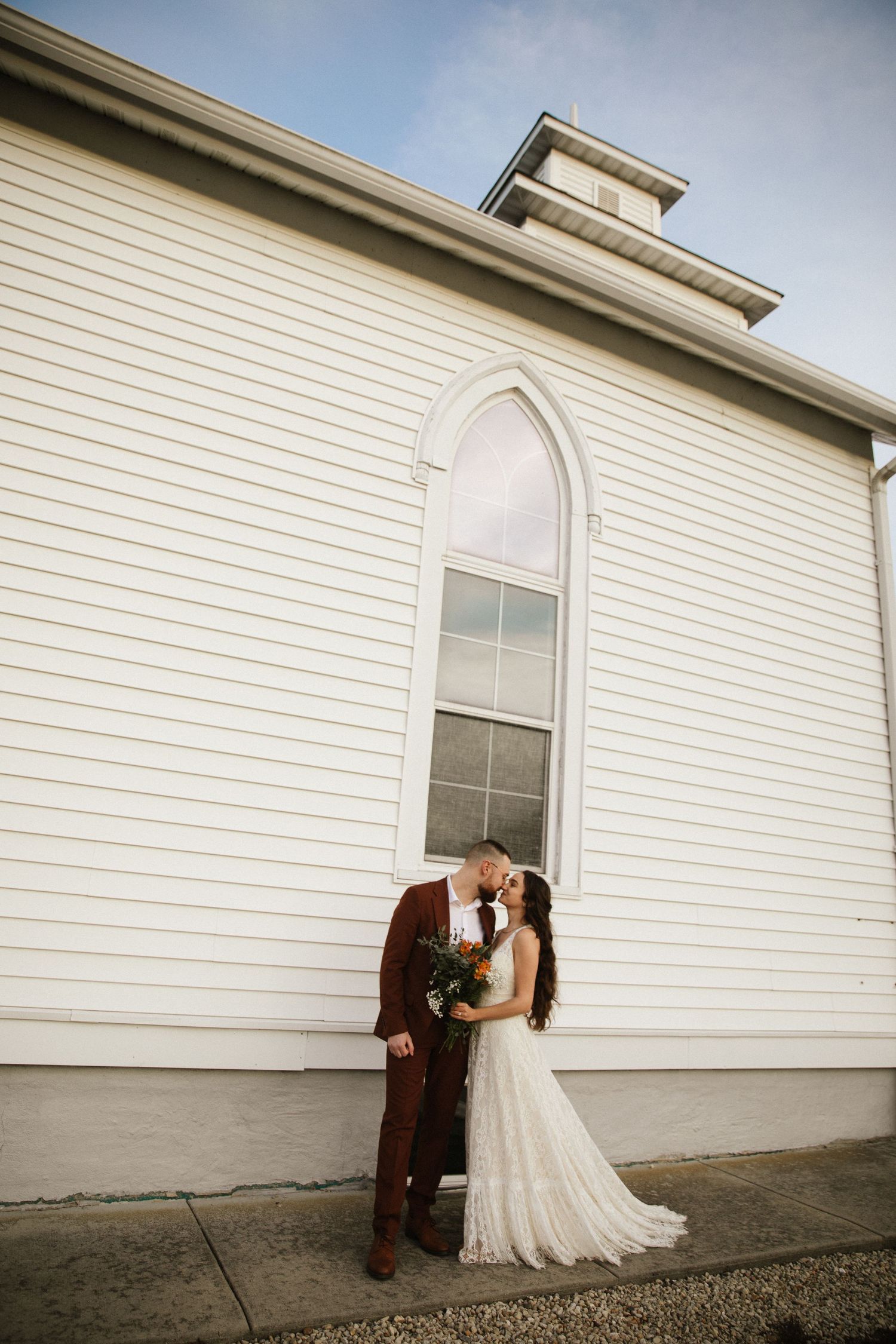 A couple shares an intimate moment against a white church building exterior.