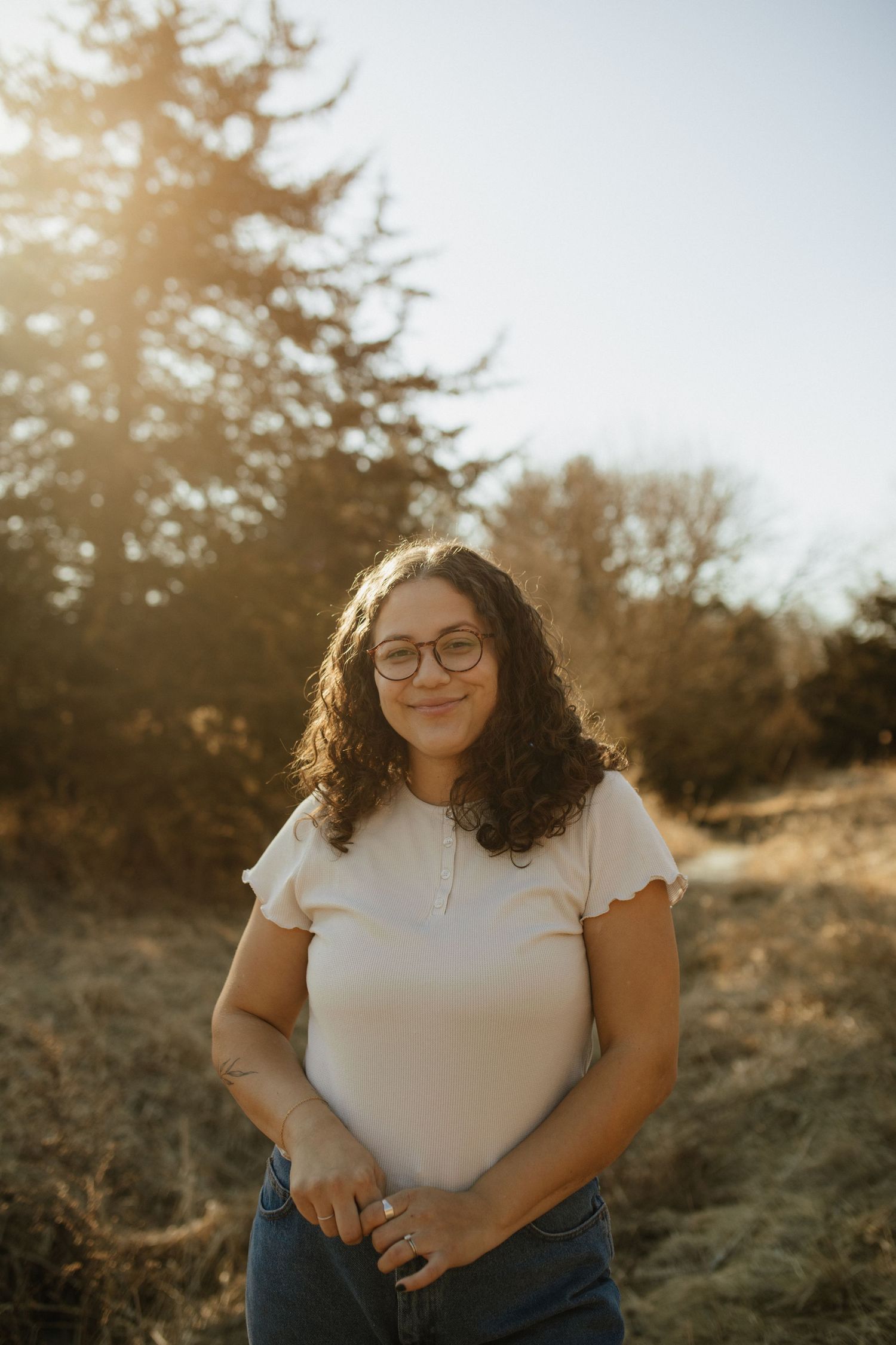 Person in white shirt sits outdoors during golden hour with natural scenery in background.