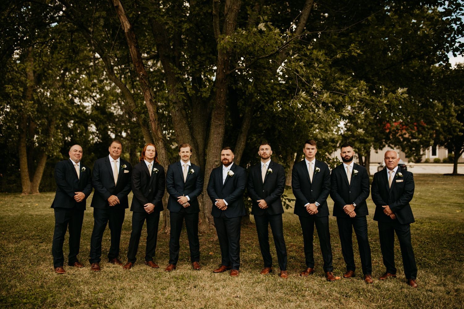Groomsmen in dark suits lined up outdoors for a formal wedding photo.