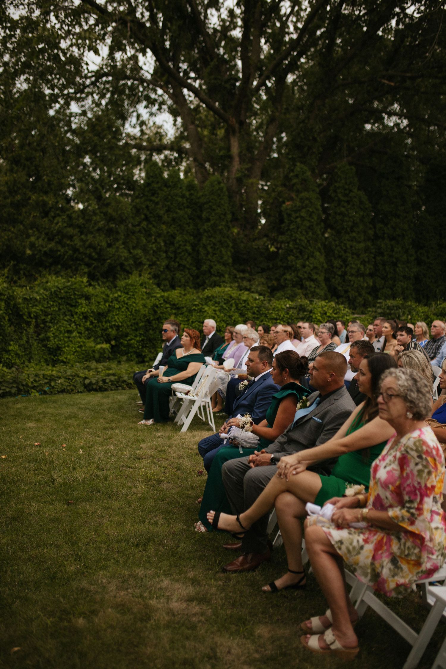 Wedding guests seated in white chairs on a grassy lawn for an outdoor ceremony.