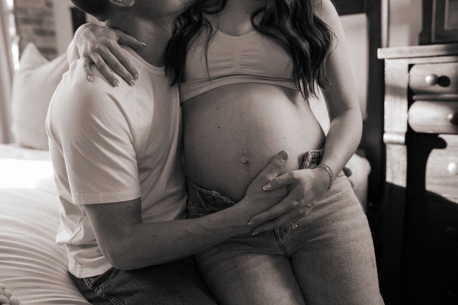 Intimate black and white photo of expectant parents touching a pregnant belly.