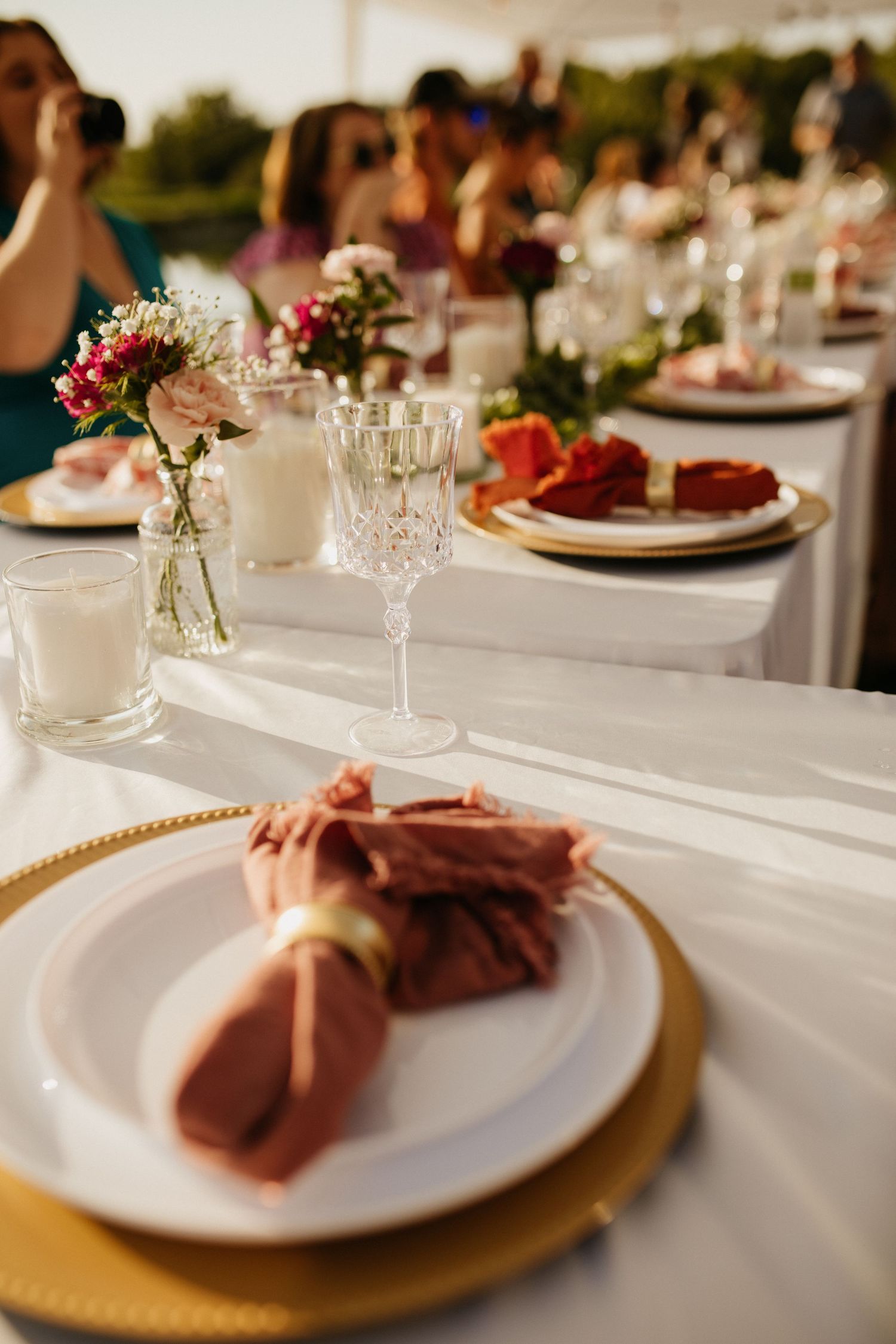 Elegant wedding reception table settings with gold chargers and pink napkins.