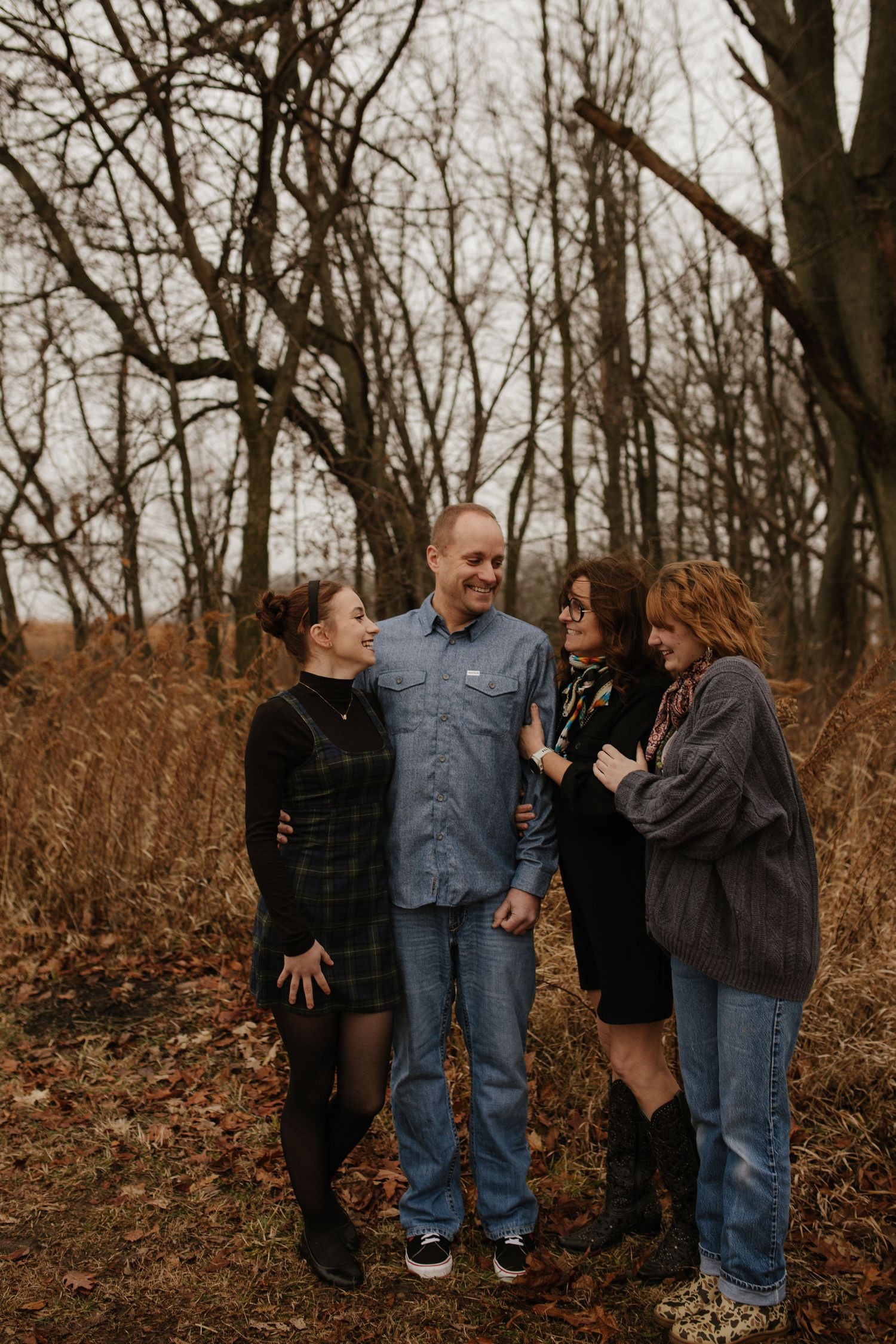 A group shares candid laughter while posing together in a wooded autumn setting.