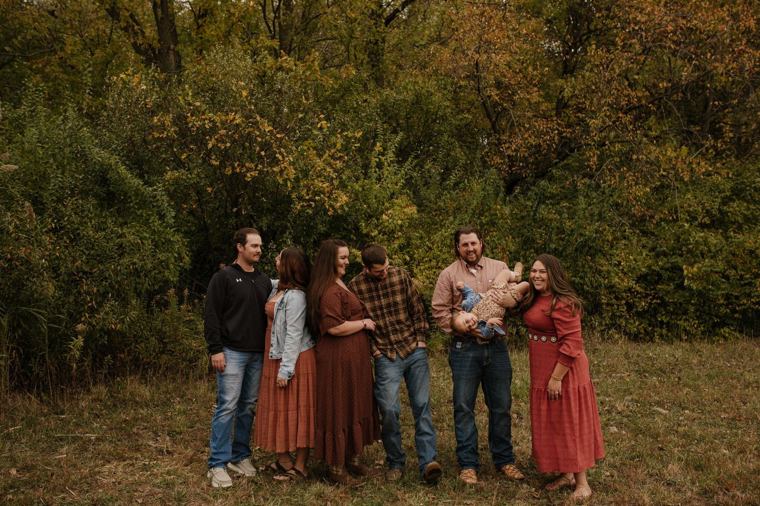 A family group poses together outdoors in autumn wearing coordinated burgundy and earth-toned clothing.