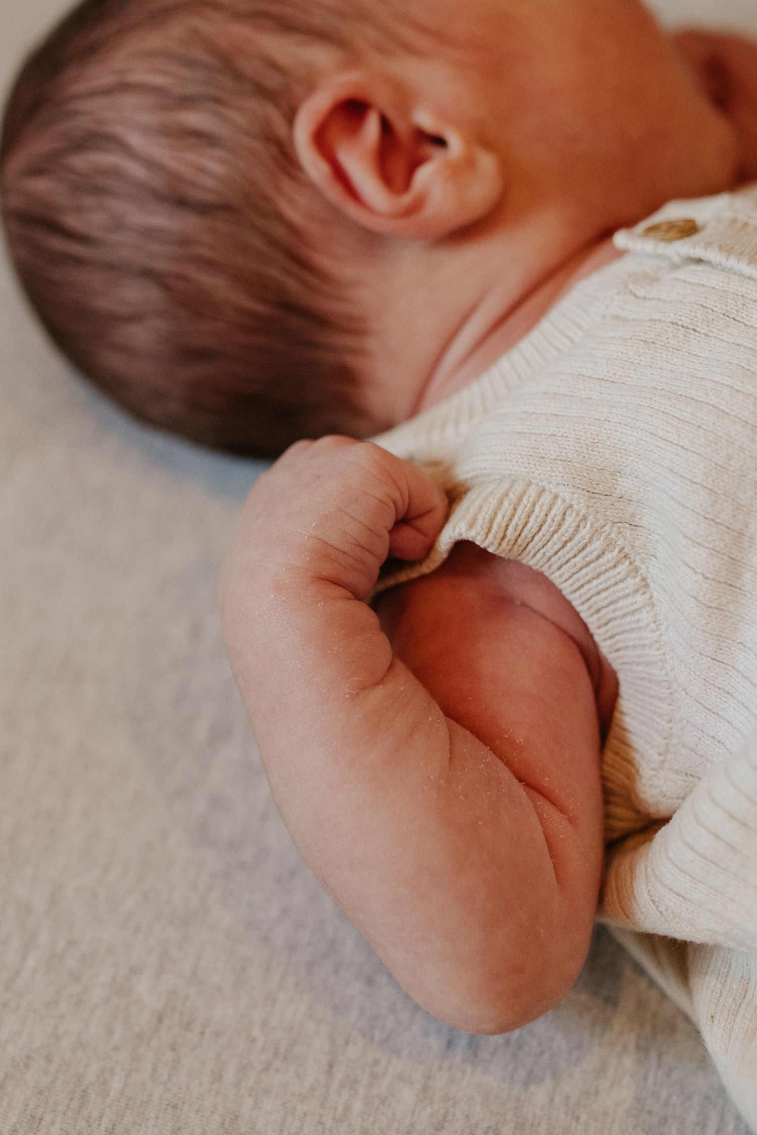 Close-up of newborn baby's ear and soft skin in white knit clothing.