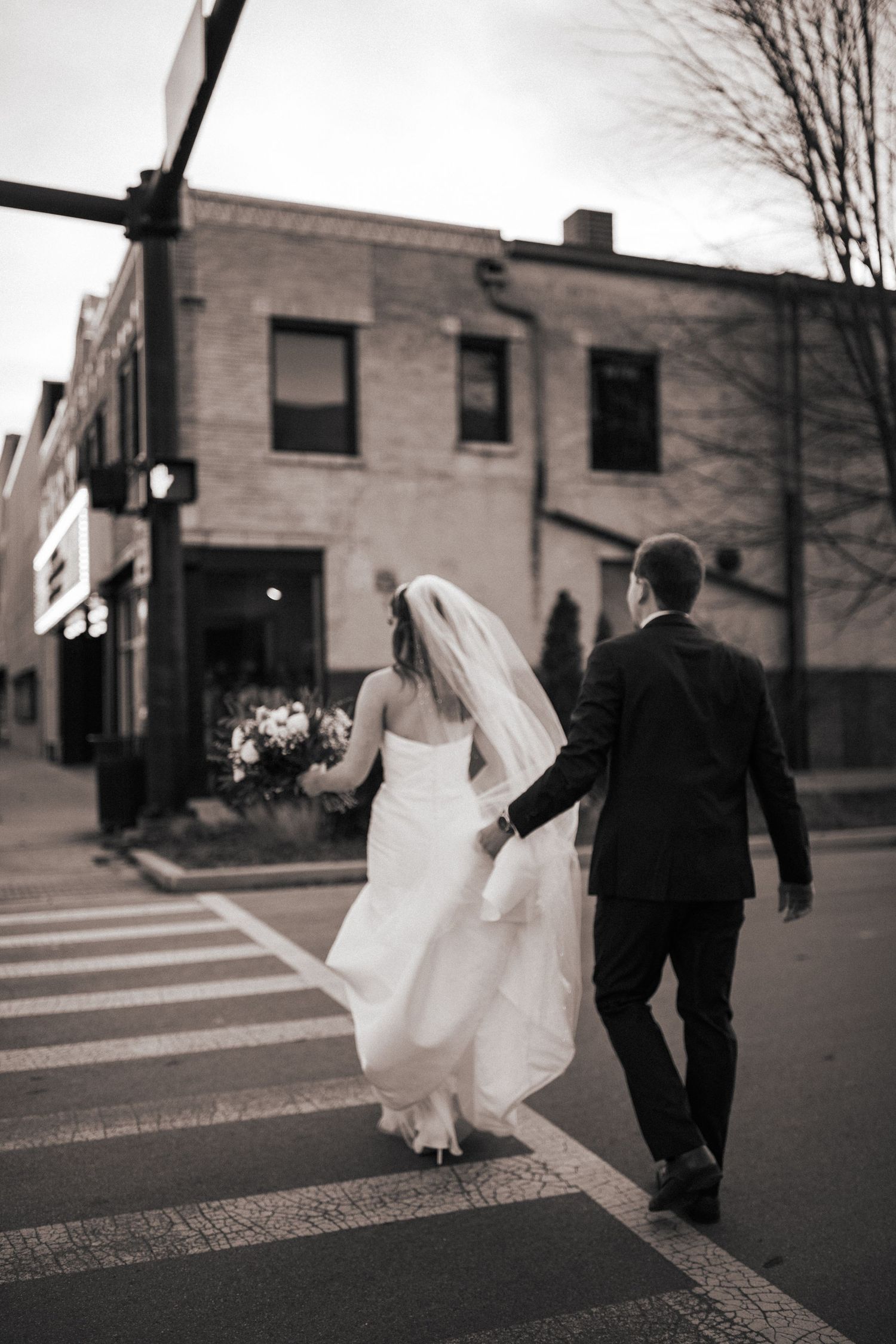 A black and white photo of newlyweds walking across a city crosswalk.