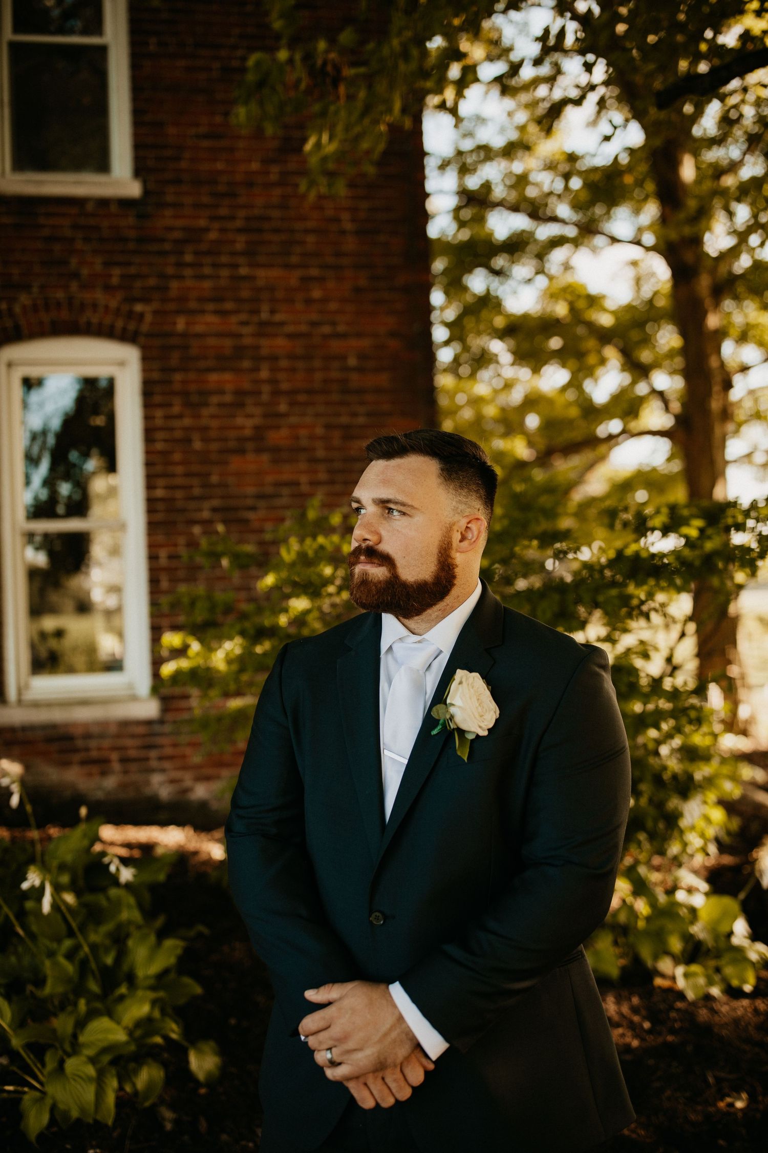 Groomsmen in black suits standing against brick wall during golden hour.