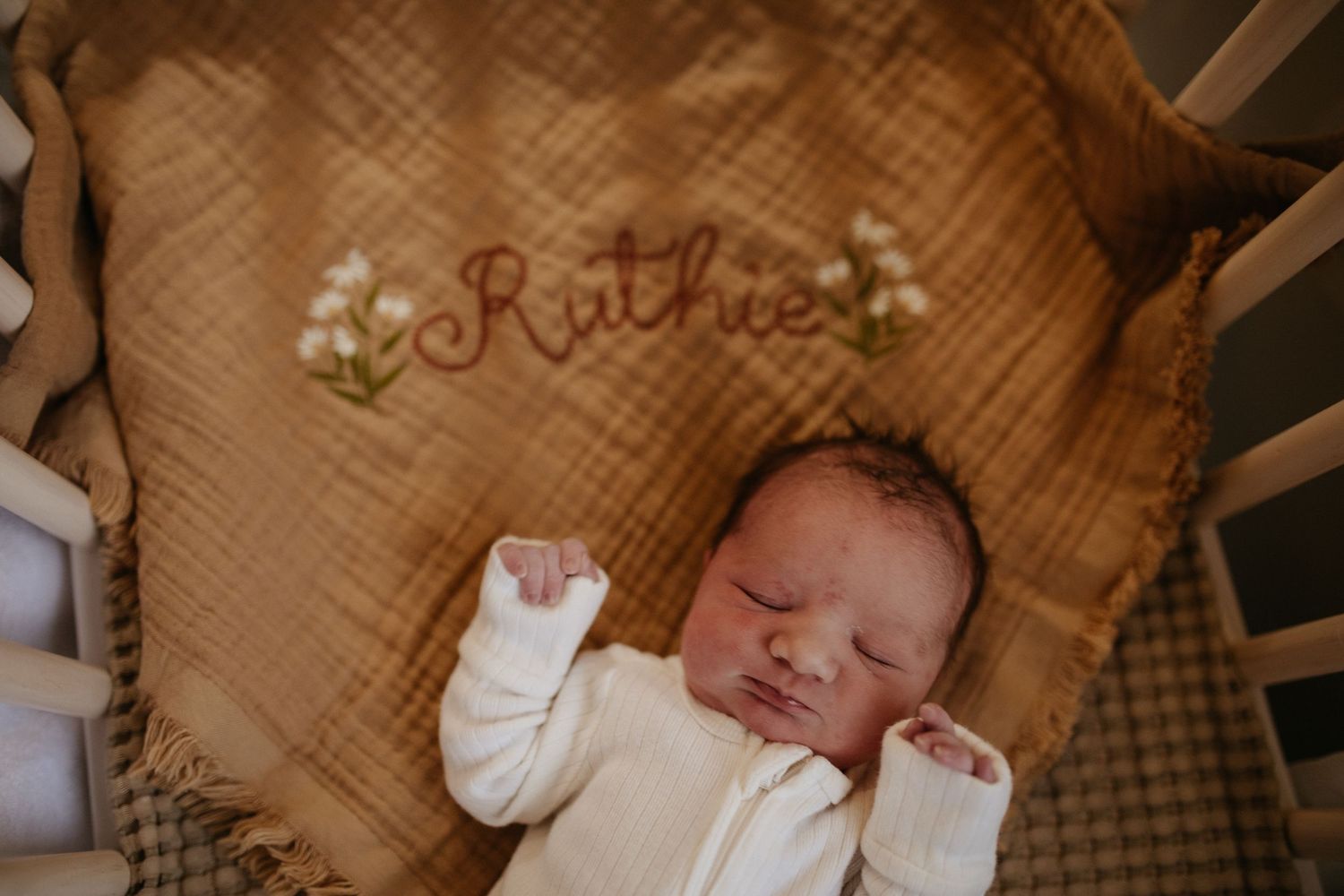 Newborn sleeping peacefully on embroidered blanket in crib.