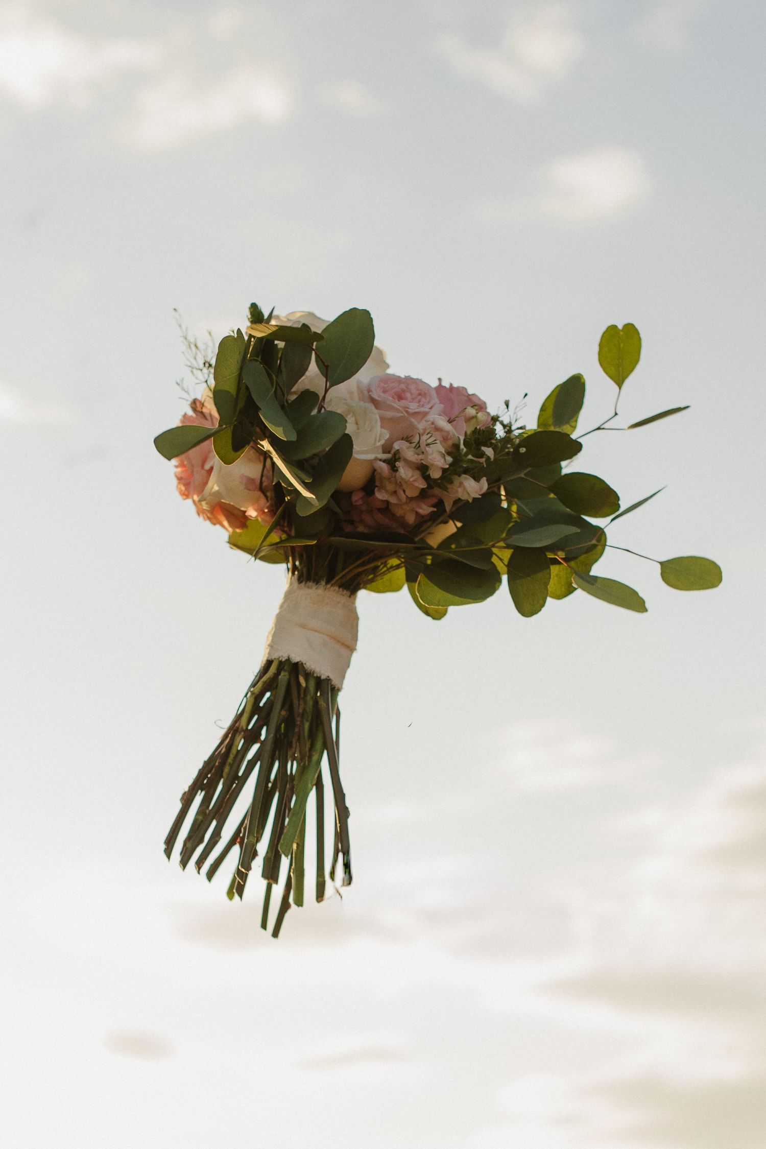 Elegant wedding bouquets with pink flowers and eucalyptus leaves against cloudy sky.