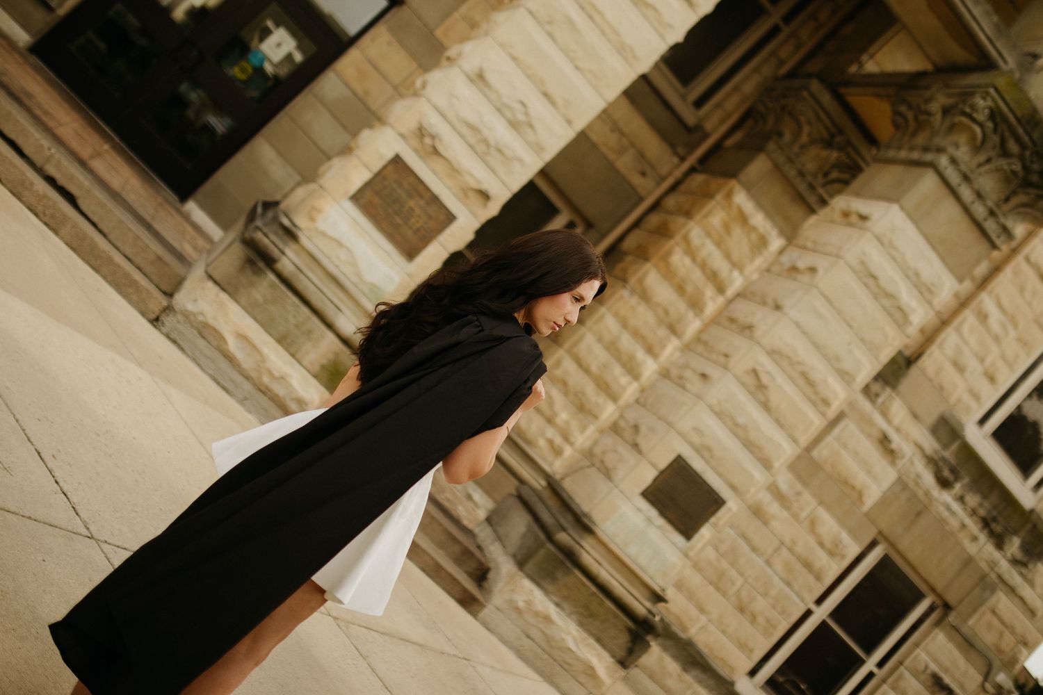 Person in dark clothing poses against architectural stone columns and walls.