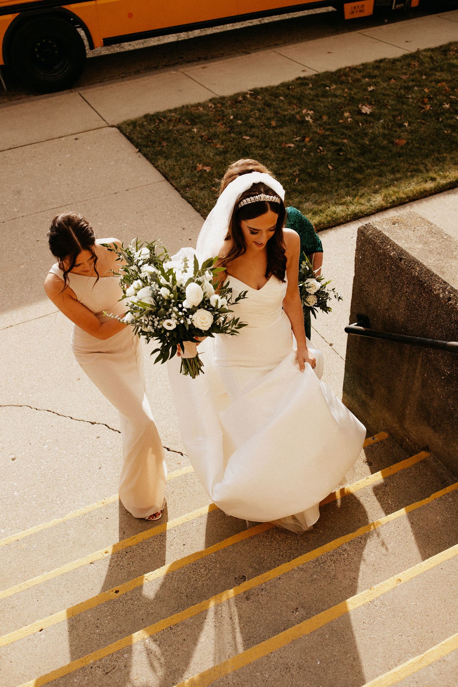 A bride and bridesmaid ascending stairs while carrying white floral bouquets.