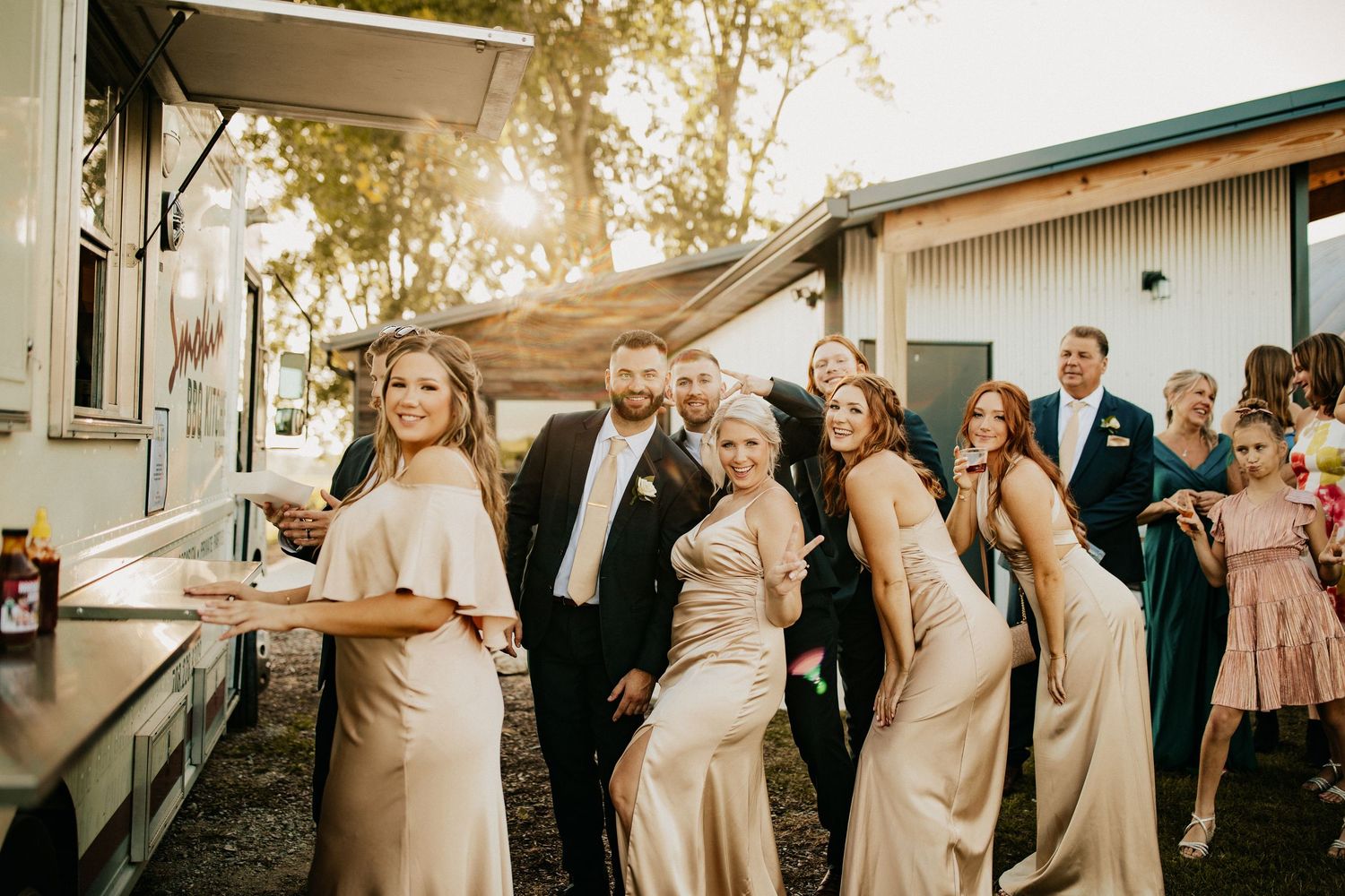 Wedding party in blush pink dresses and dark suits posing outdoors at sunset.