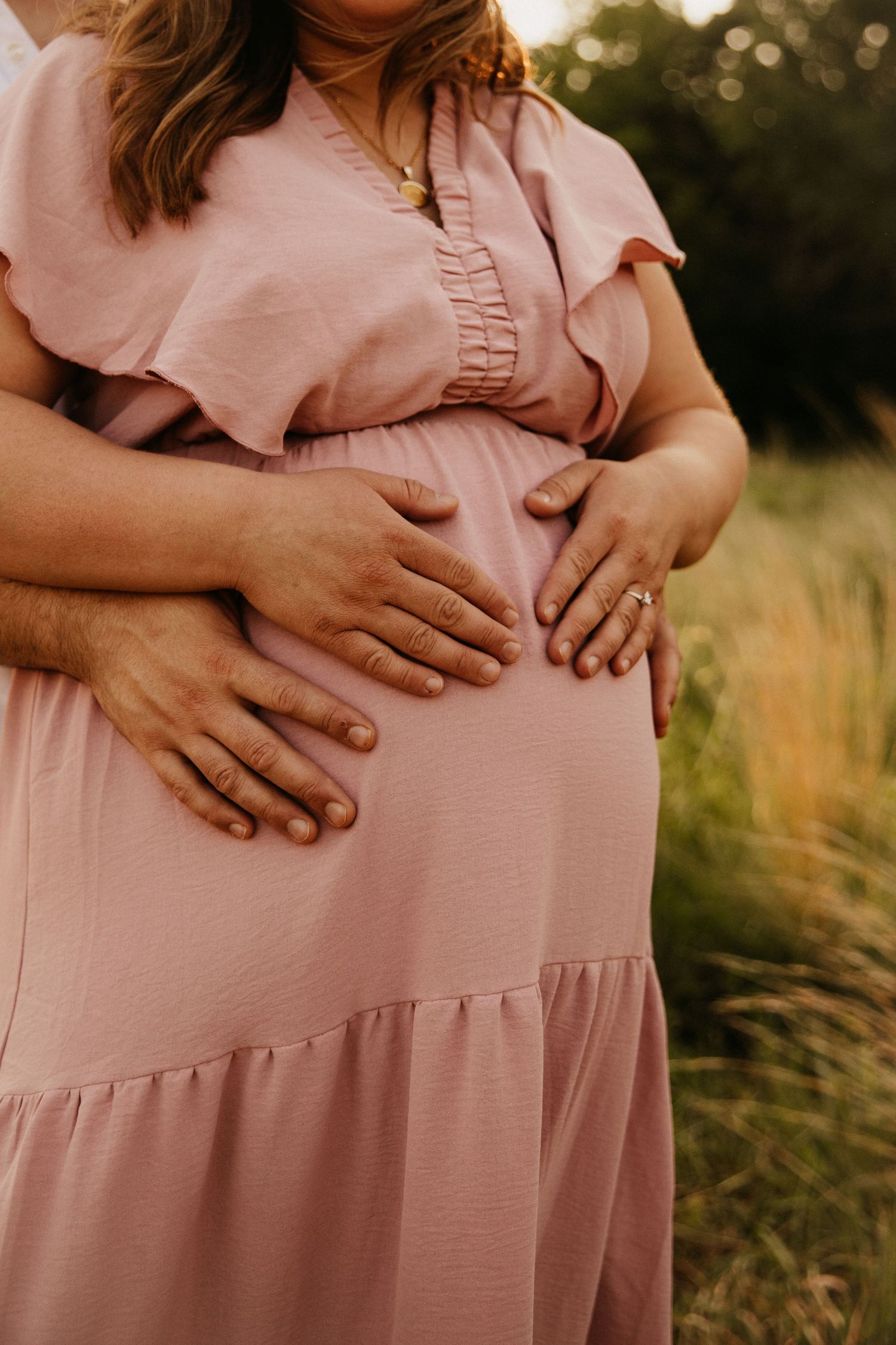 Close-up of hands cradling pregnant belly in pink dress.