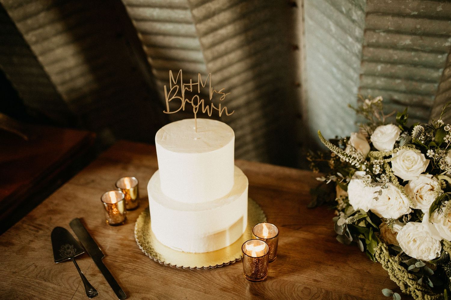 Elegant white wedding cake decorated with fresh flowers and greenery on a rustic wooden table.
