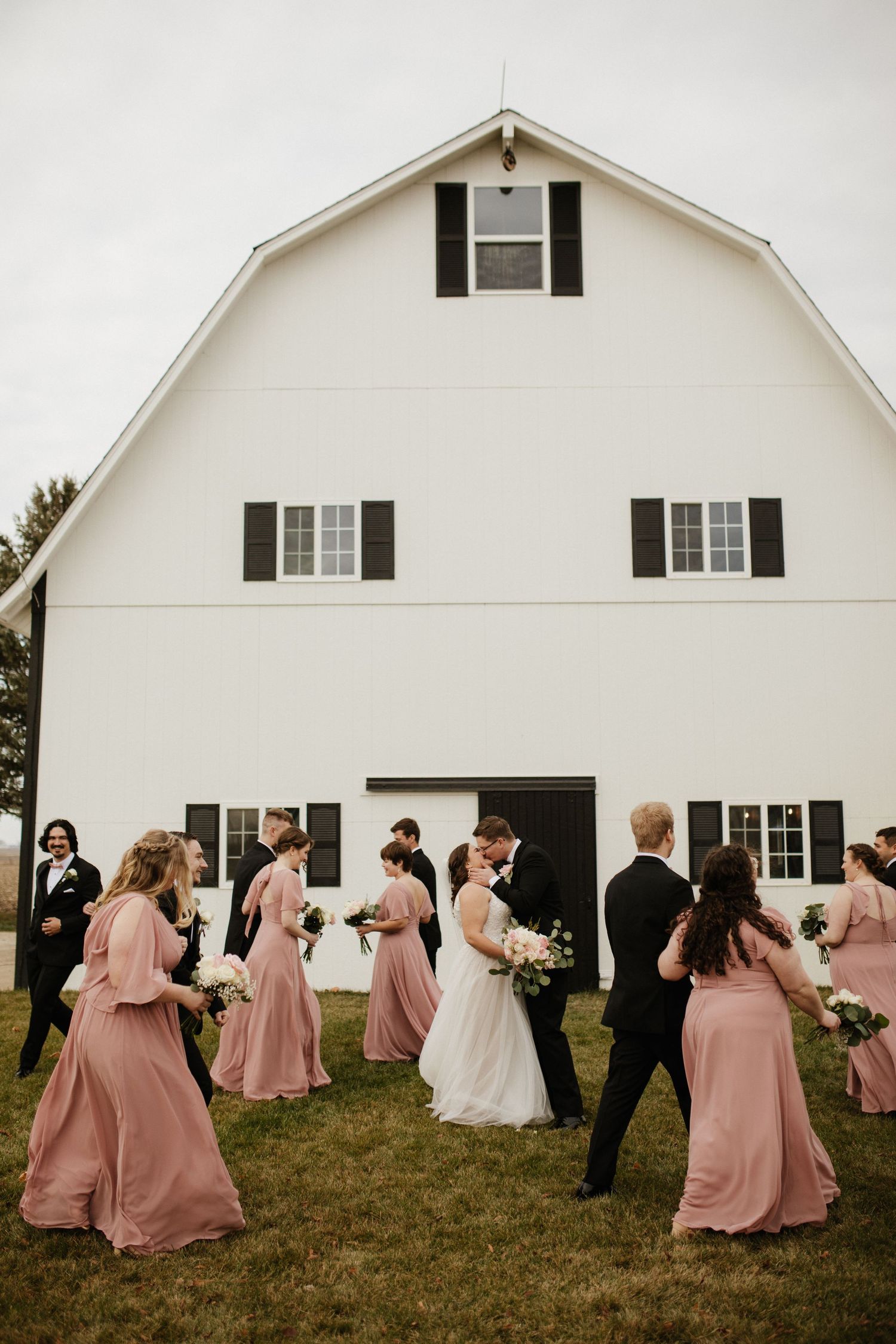 Wedding party poses in front of a classic white barn with black shutters.