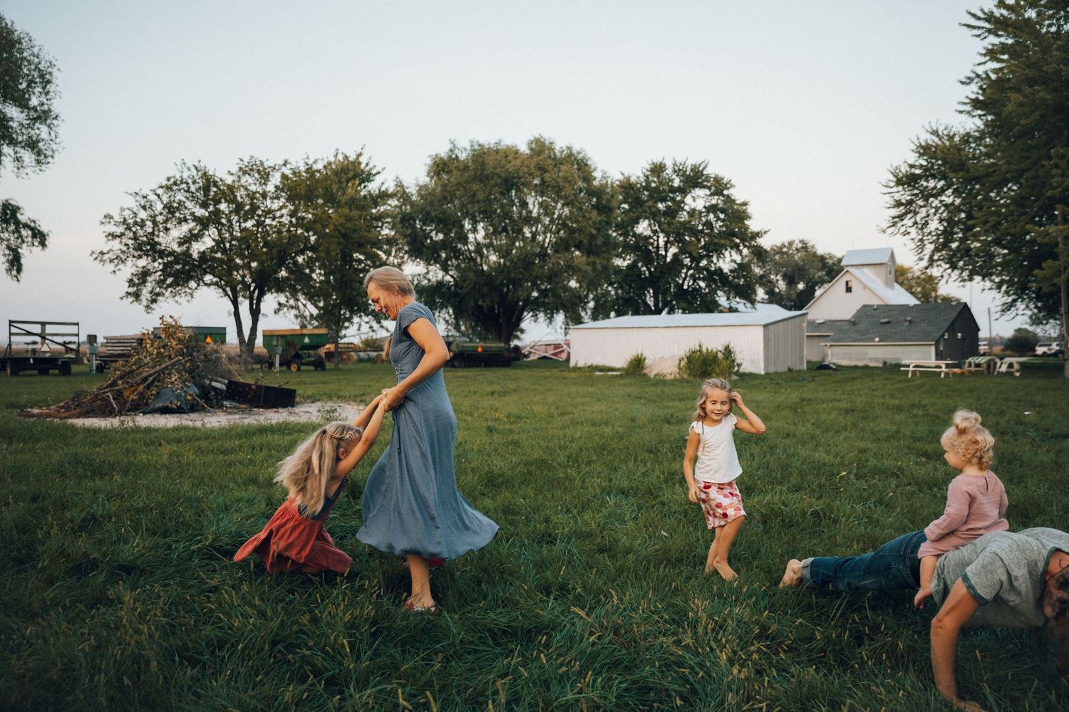 Children playing and rolling down a grassy hill at sunset in a rural setting.