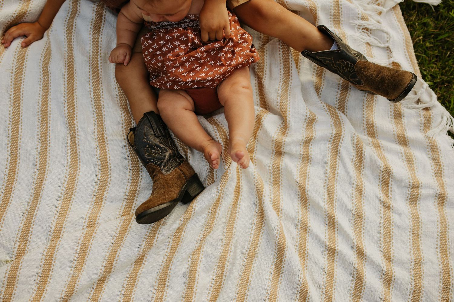 Small feet in cowboy boots rest on a striped blanket during an outdoor picnic.