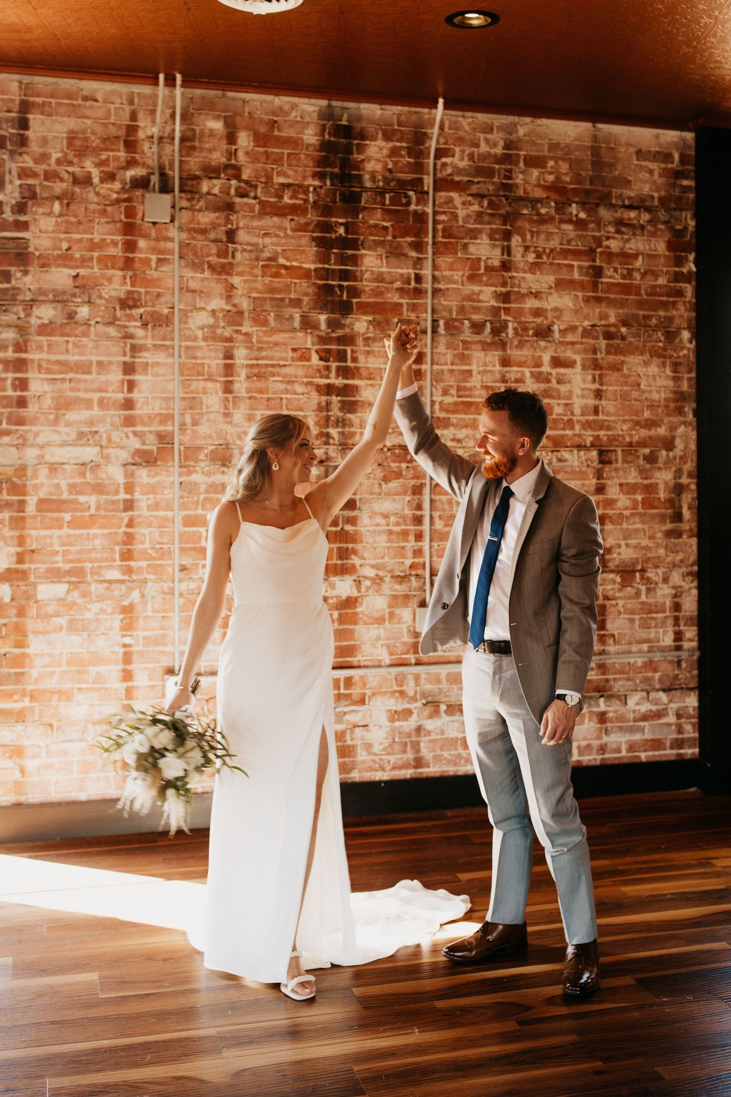 A celebratory dance moment against an exposed brick wall in warm lighting.