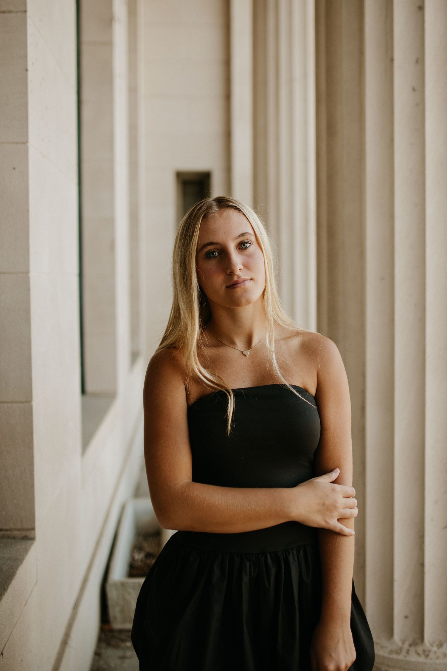 Person in black dress poses between white architectural columns.
