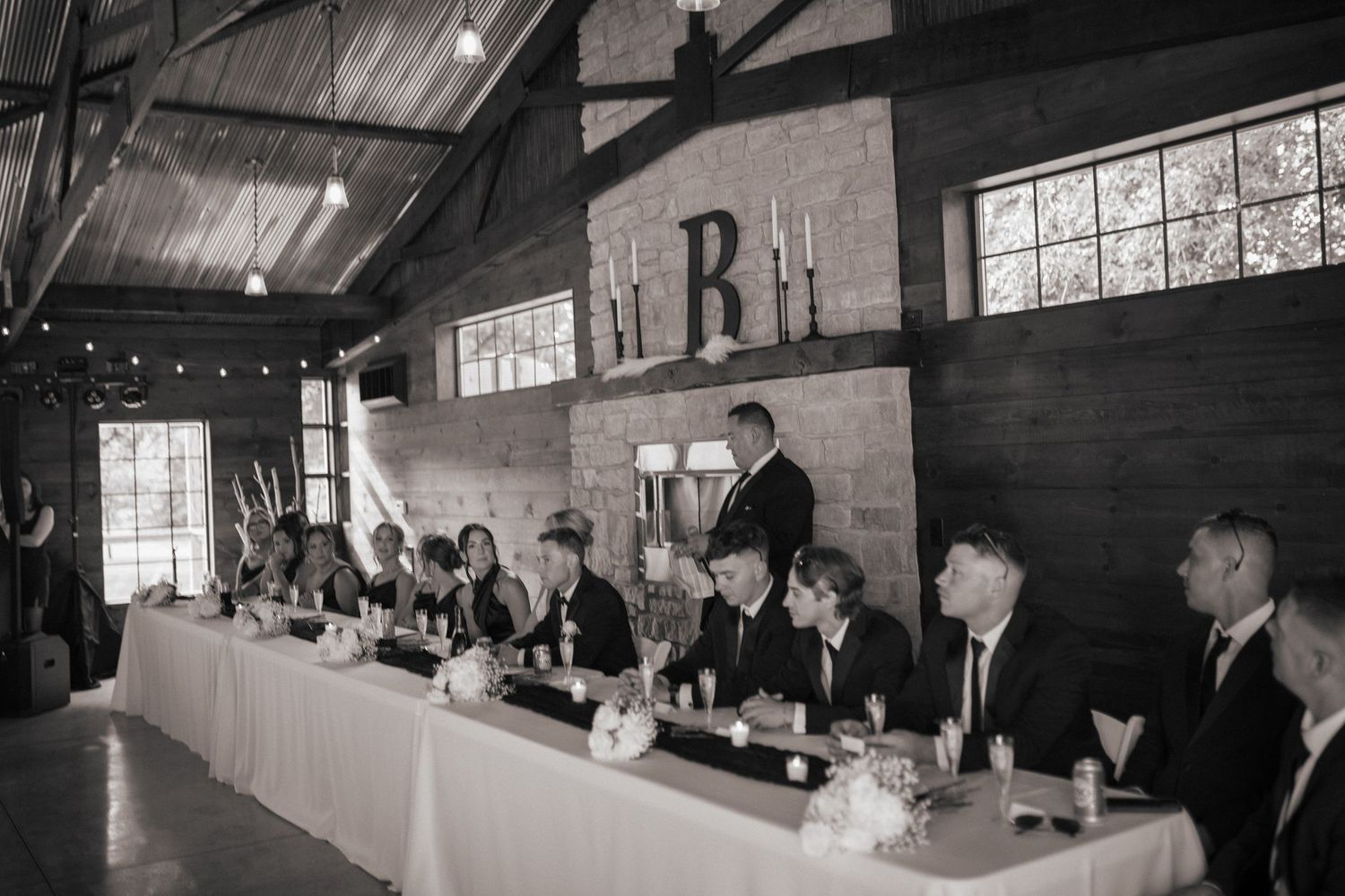 Wedding reception setup in rustic barn venue with exposed wooden beams and windows.