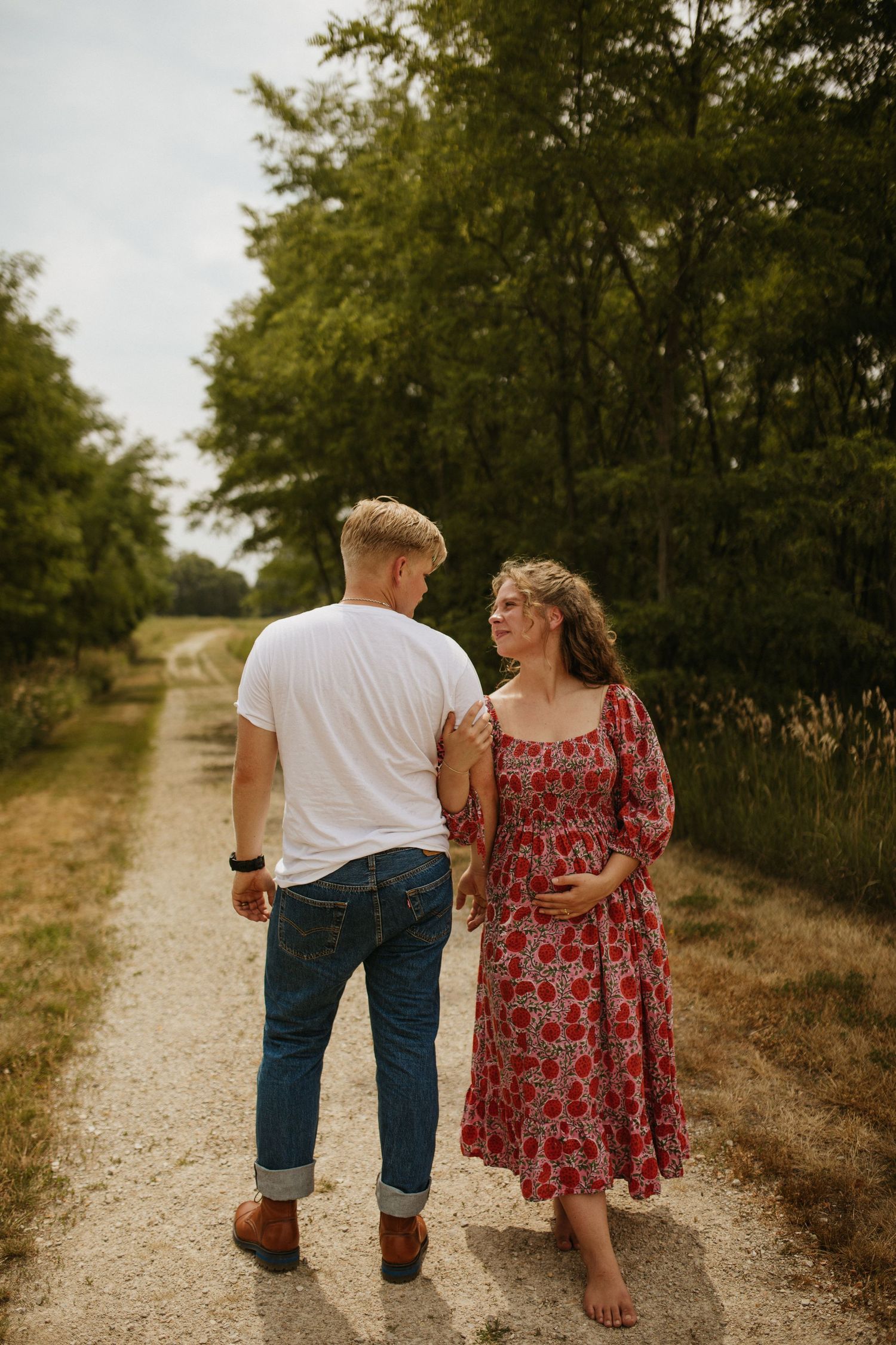 Couple walking hand in hand down gravel path surrounded by greenery.
