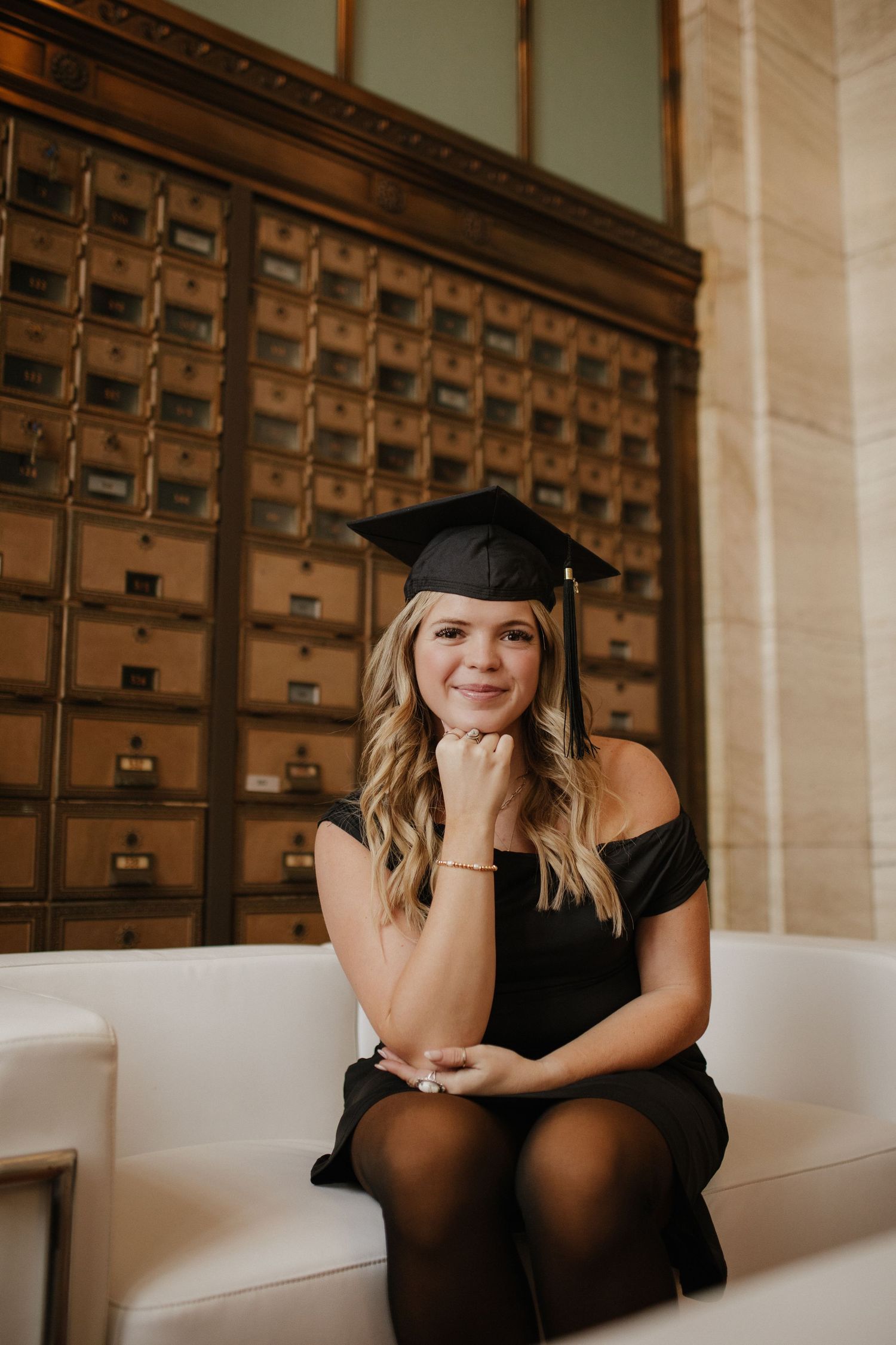 Graduate seated on white couch in front of vintage wooden card catalog.