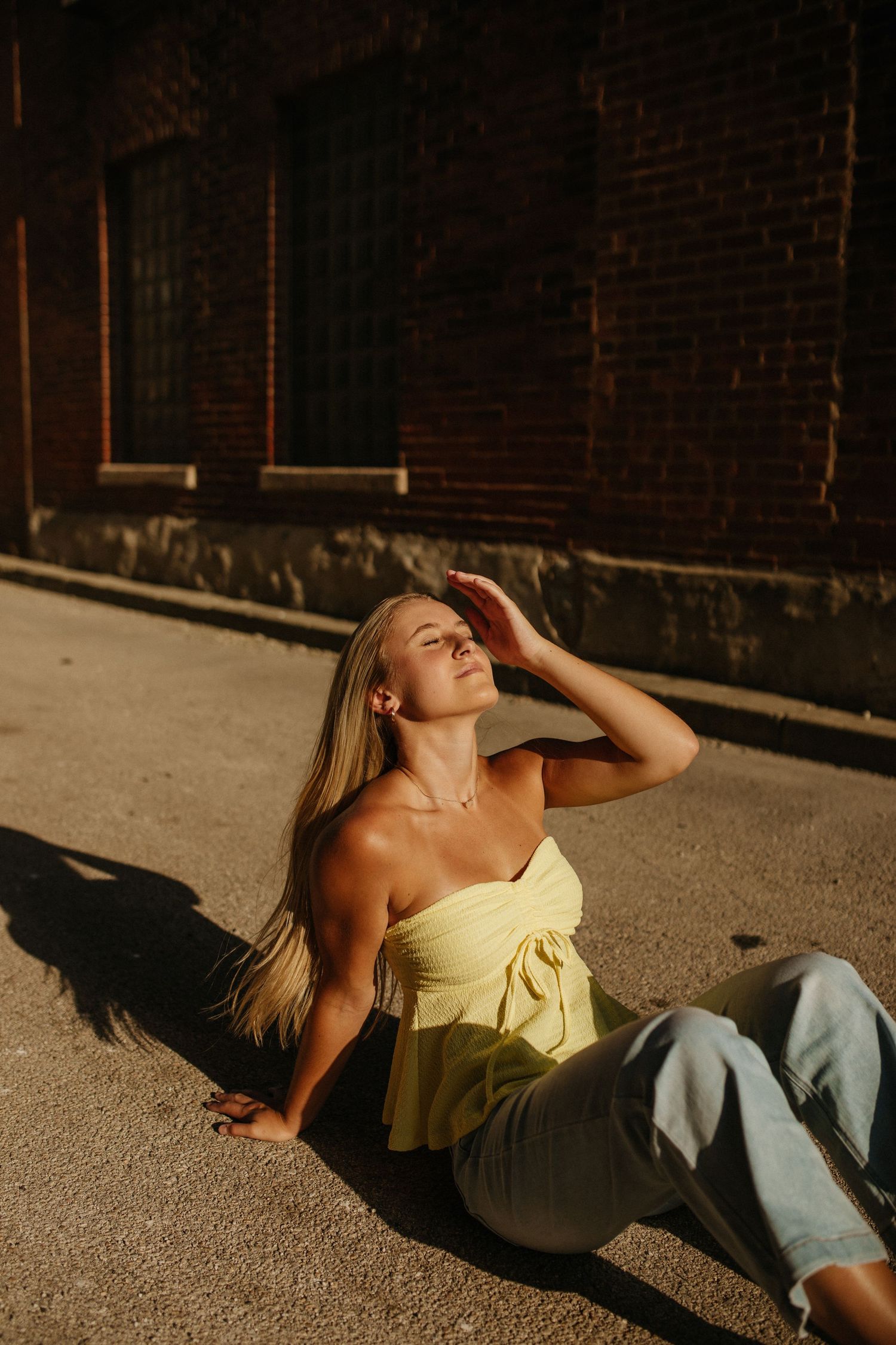 Woman in yellow top basking in golden sunlight against brick wall.